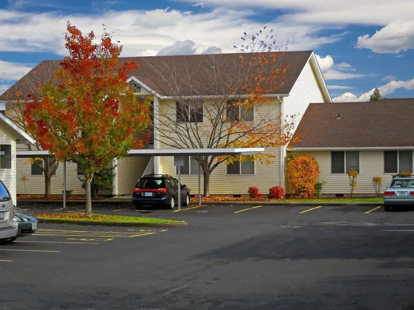 Suburban apartment building with autumn trees and parked cars in the lot