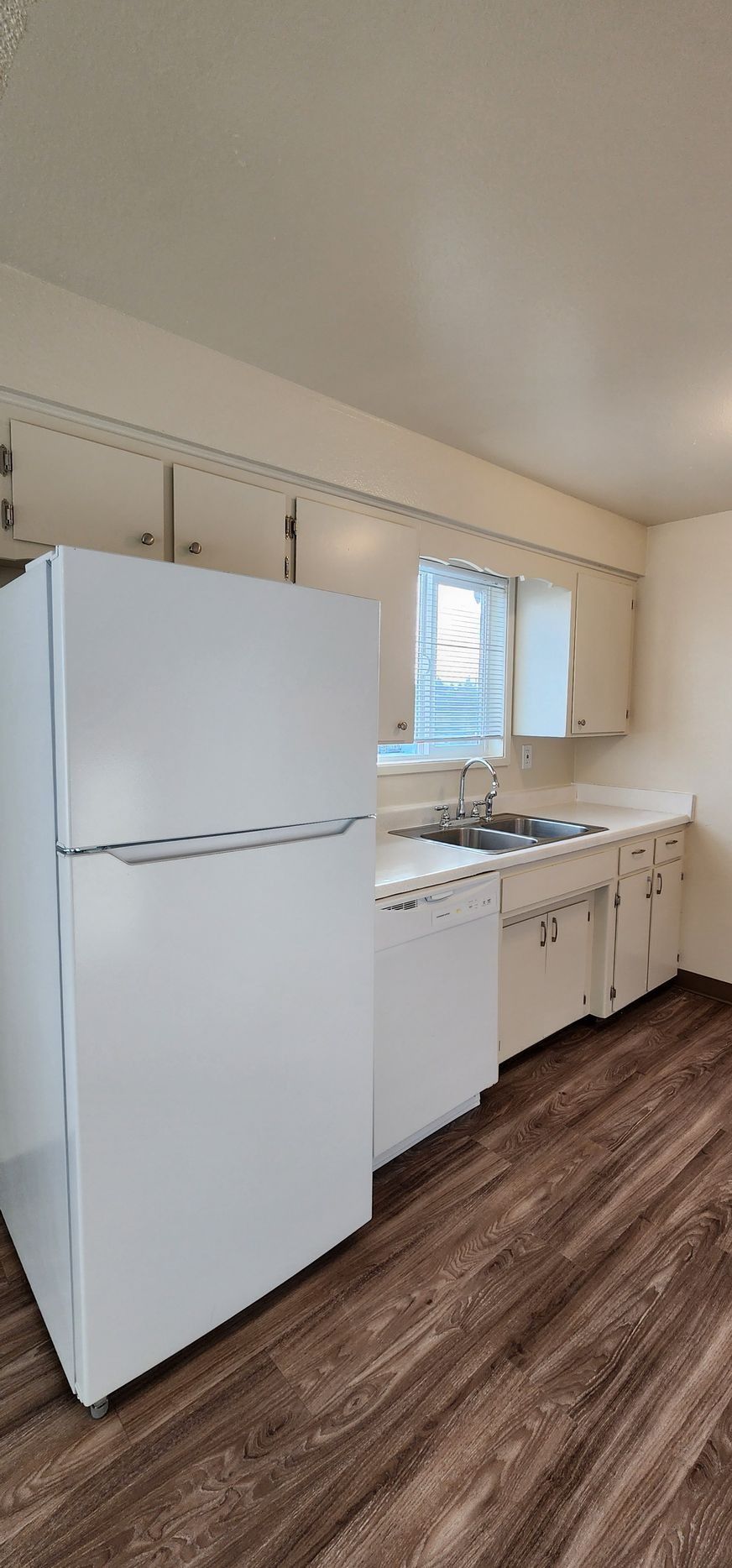 Small white kitchen with refrigerator, stove, sink, and wood-look flooring.