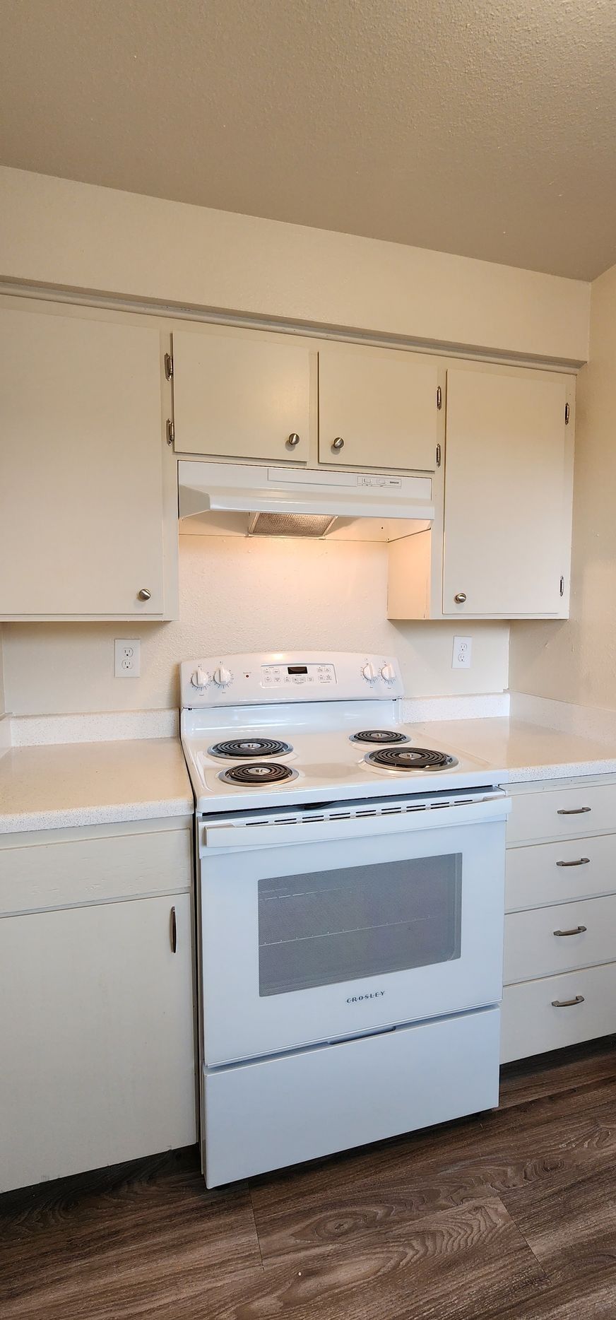 Small white kitchen with stove, oven, cabinets, and wood floor, lit by warm under-cabinet light