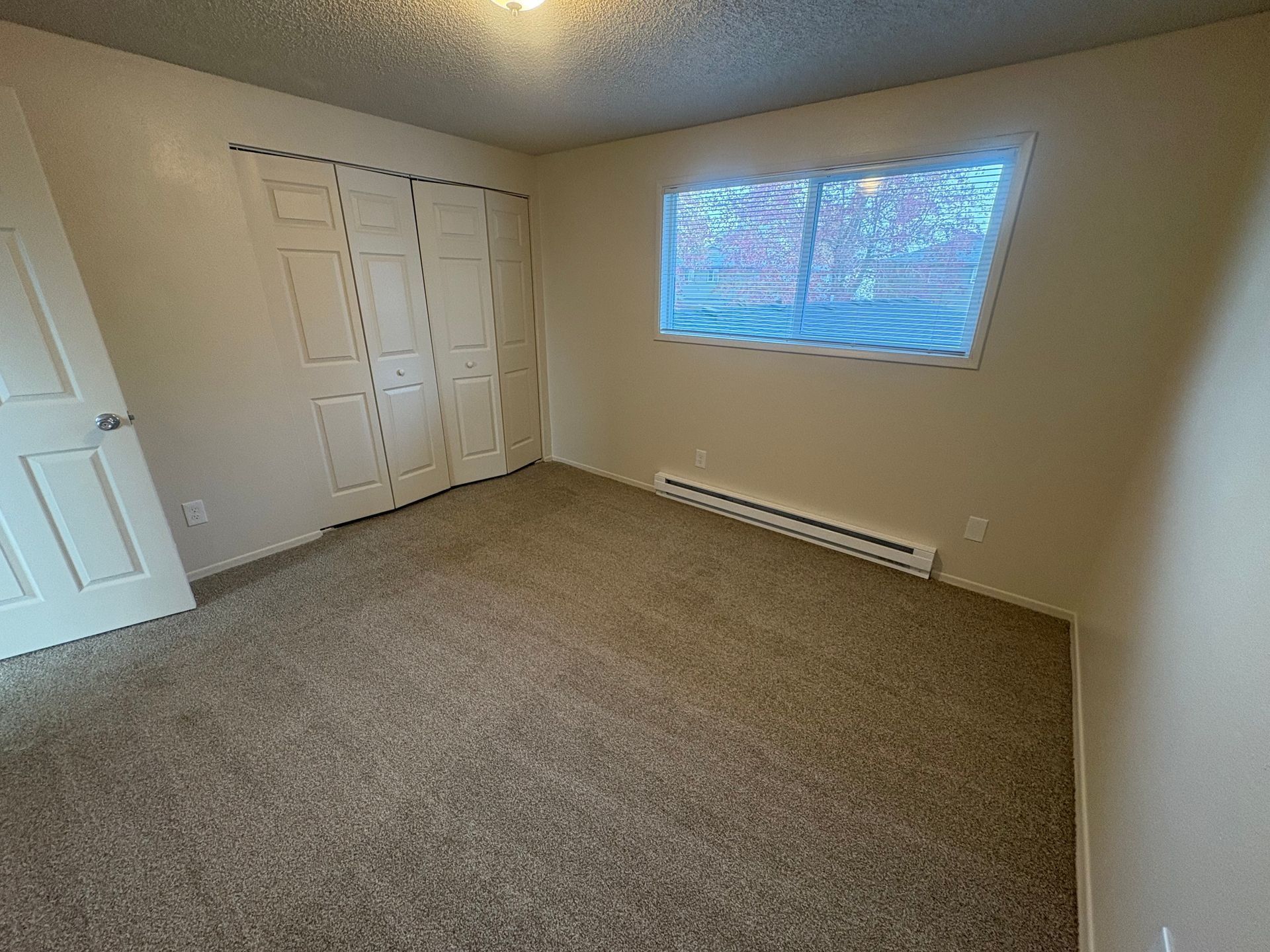 Empty beige bedroom with carpet, closet doors, and a window