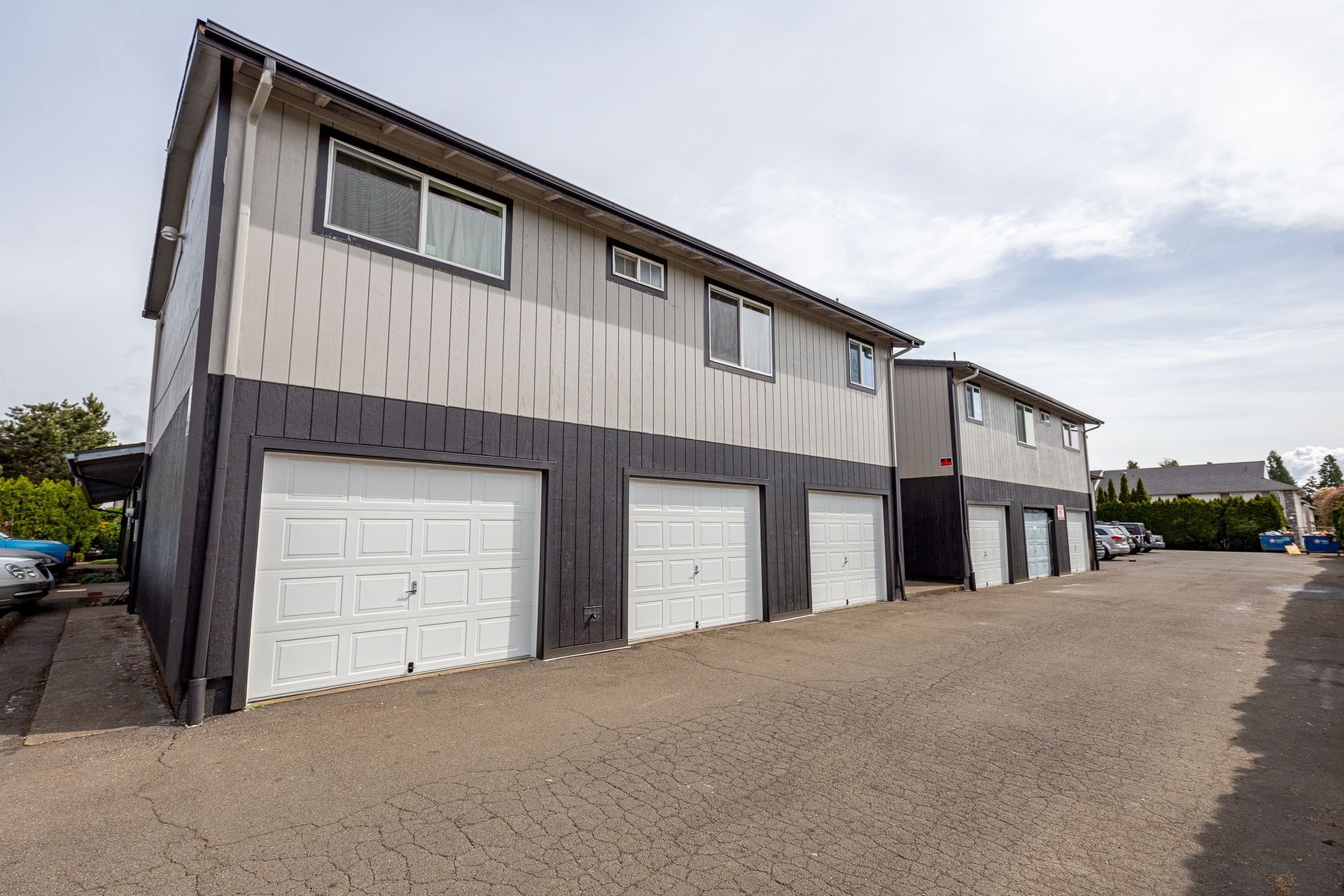 Two-story apartment building with attached garages and gravel parking area under cloudy sky