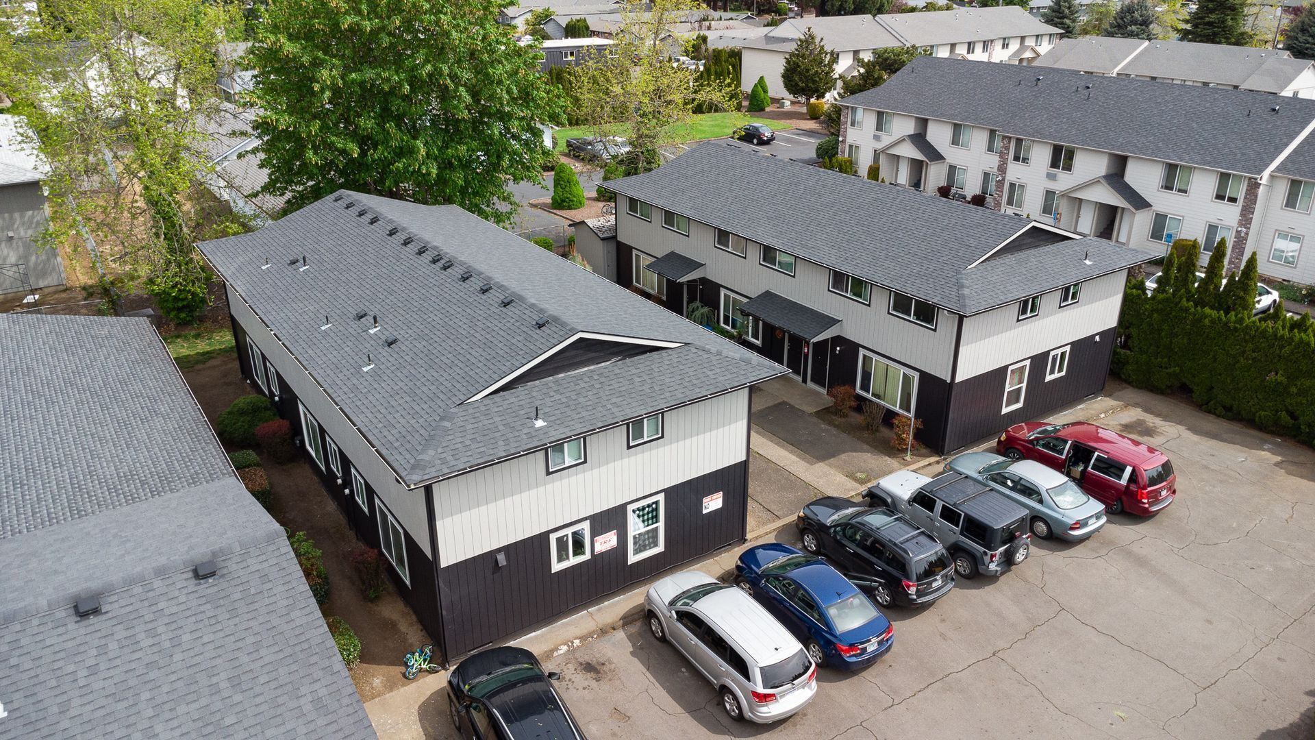 Aerial view of apartment buildings with a parking lot full of parked cars and trees nearby