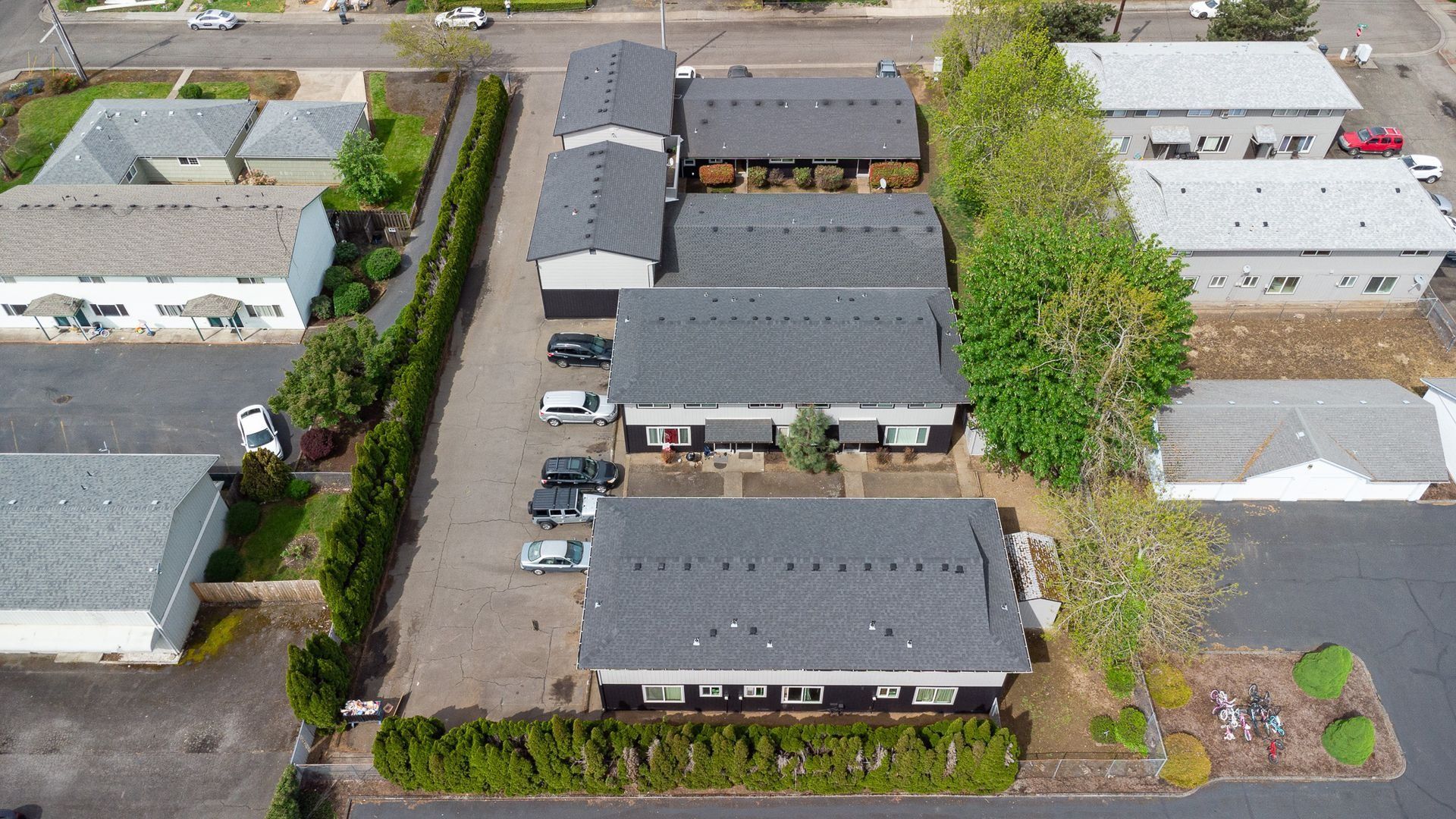 Aerial view of a suburban apartment complex with parked cars, trees, and surrounding streets.