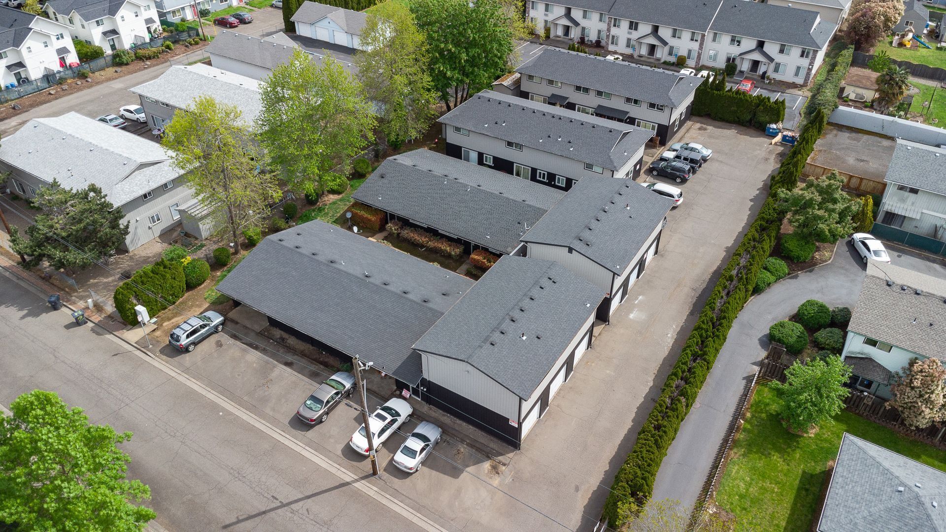 Aerial view of gray industrial buildings and parked cars in a small commercial lot
