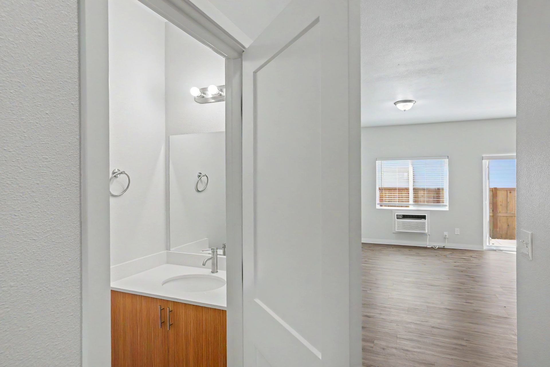 Hallway view into a small bathroom and a bright empty living room with carpet and windows
