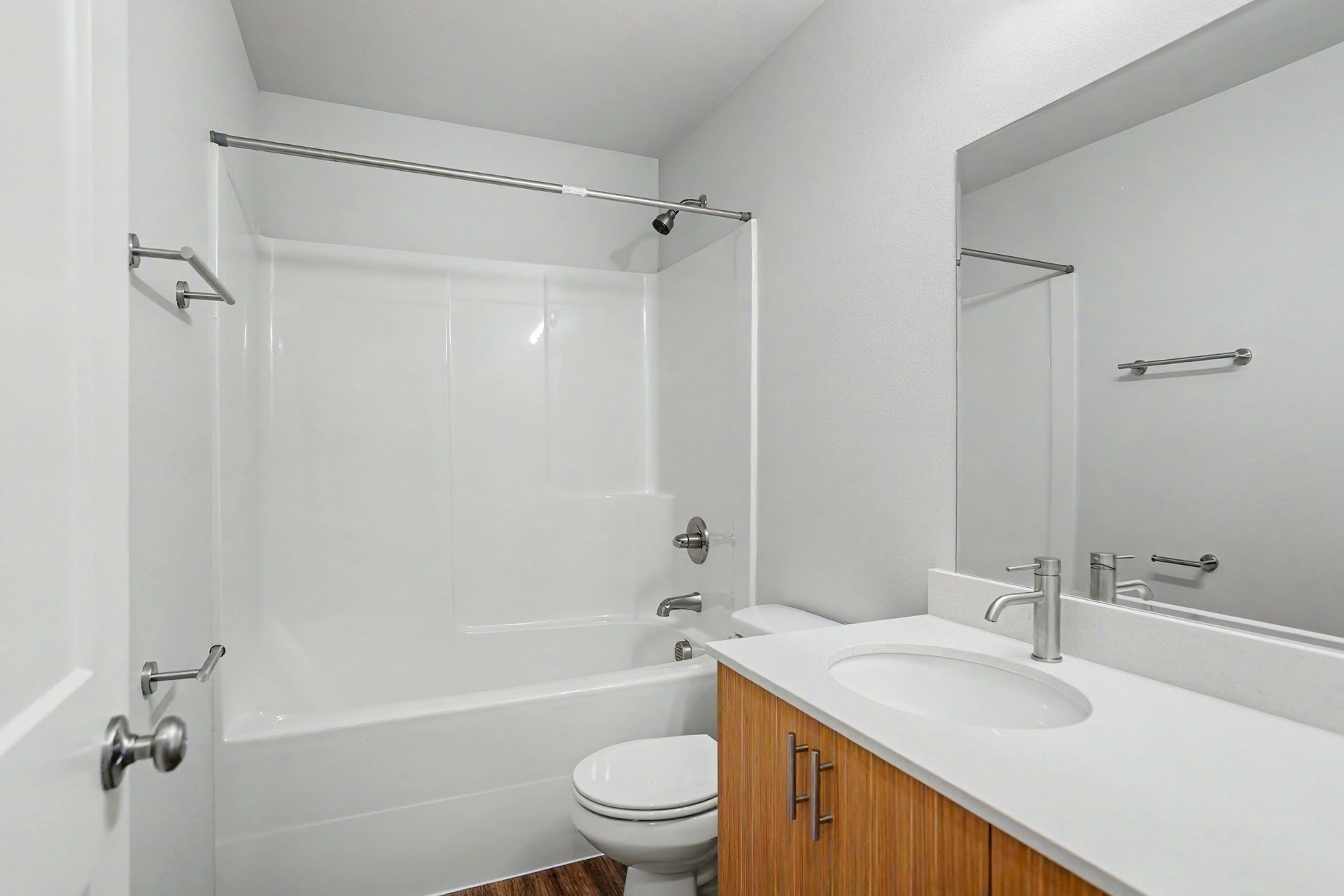 Clean white bathroom with tub-shower, toilet, and wood vanity with sink and mirror.