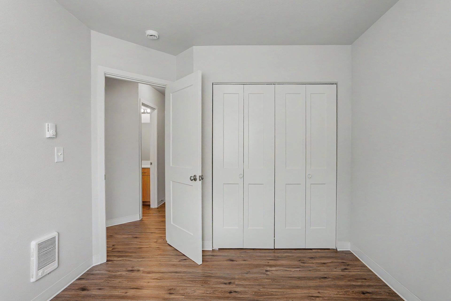 Empty white bedroom with wood floors, open door, and closed closet doors