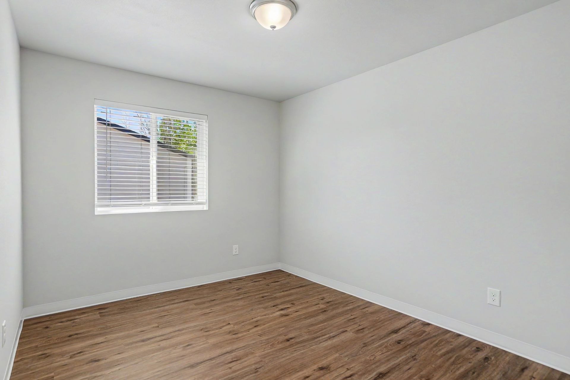 Empty white room with wood flooring, window blinds, and a ceiling light