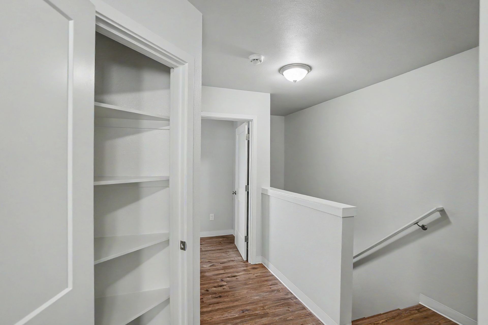 Bright hallway with white walls, built-in shelves, and a staircase with a metal handrail.