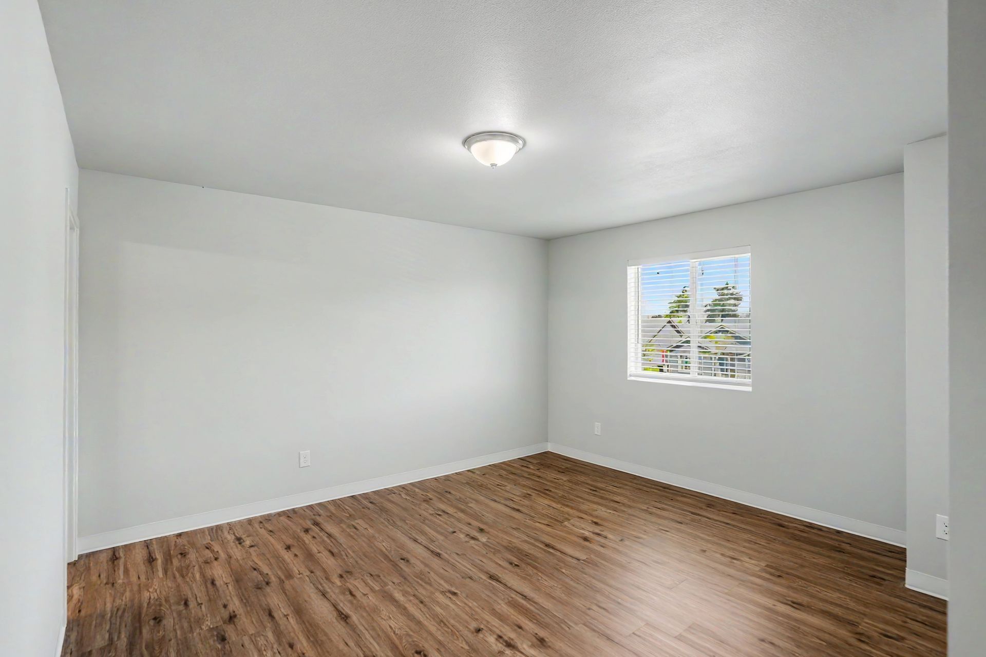 Empty white room with wood floor and a small window letting in daylight.