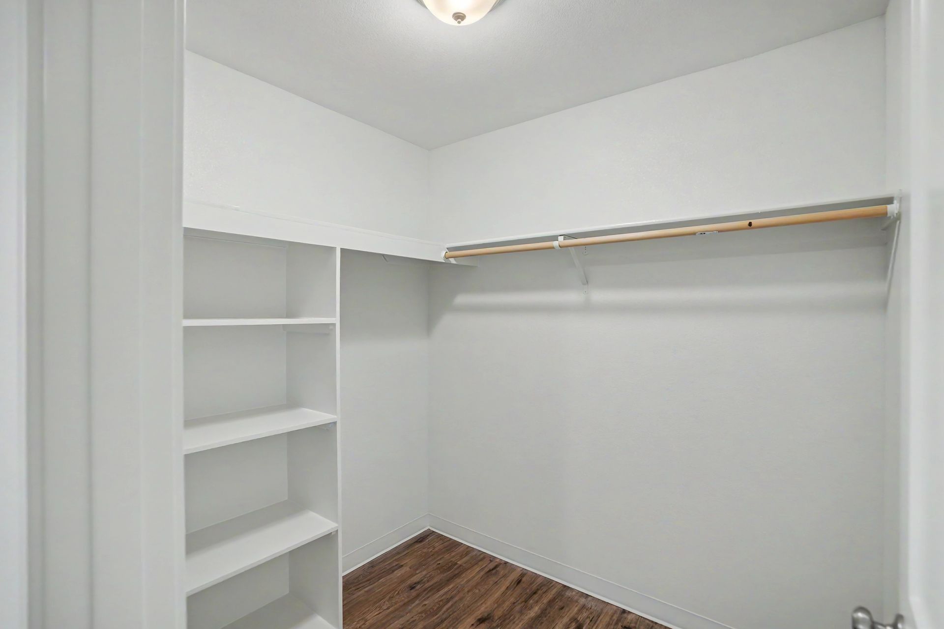Empty white walk-in closet with shelves, hanging rod, and wood floor