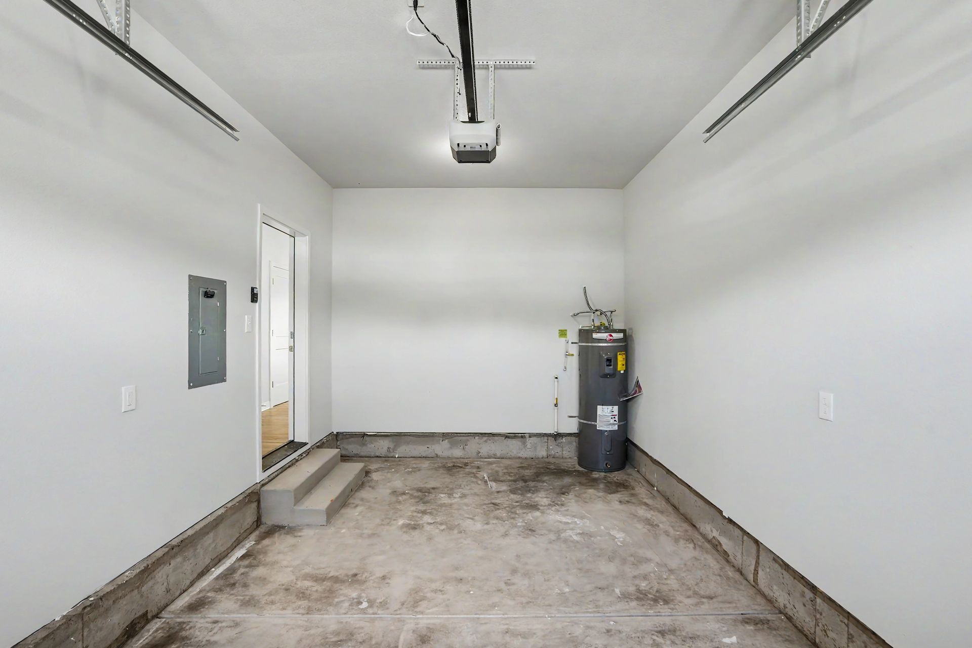 Empty white garage with bare concrete floor, ceiling light, and a utility cart near the back wall.