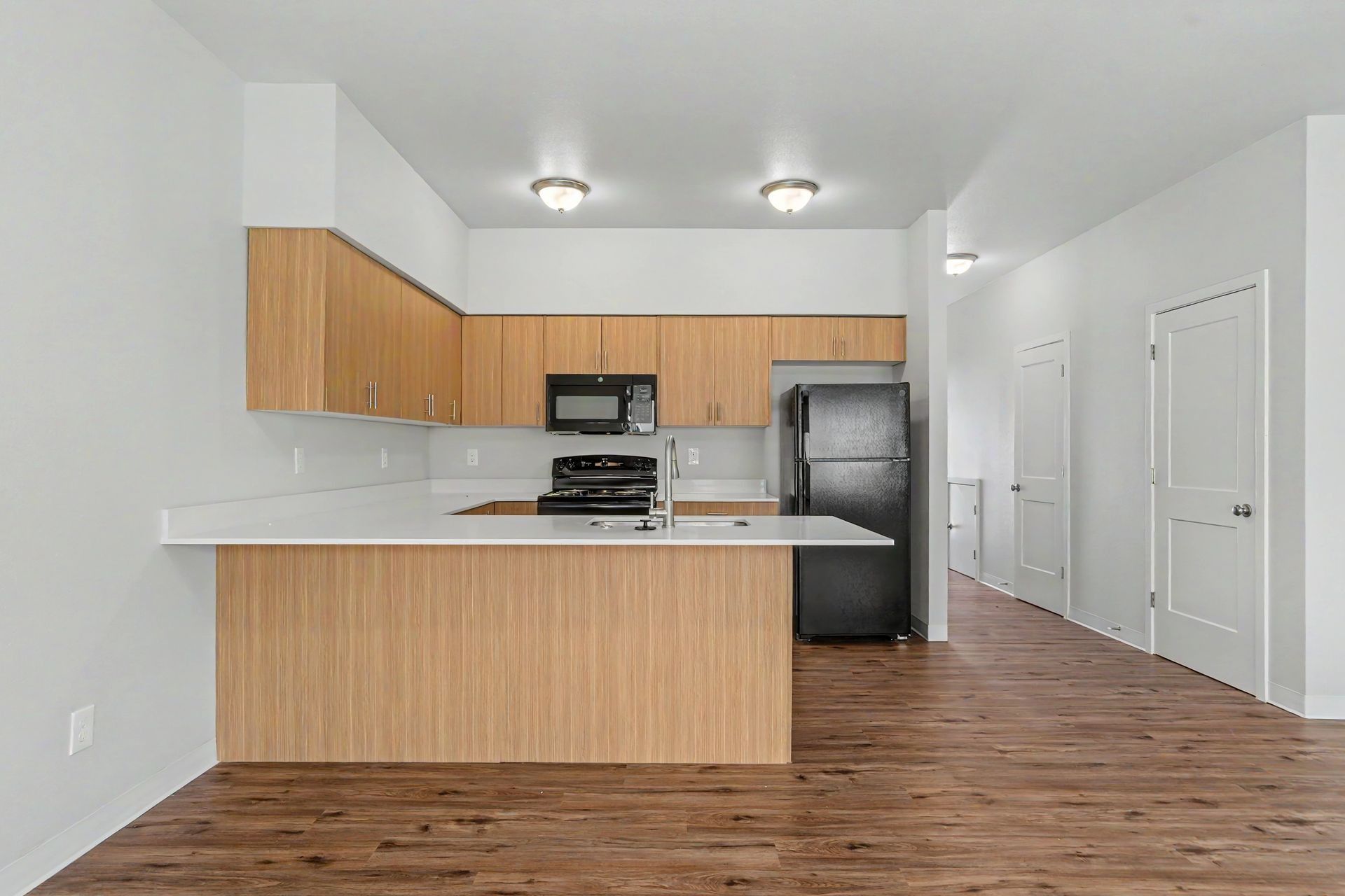 Empty modern kitchen with wood cabinets, stainless appliances, and wood-look flooring.