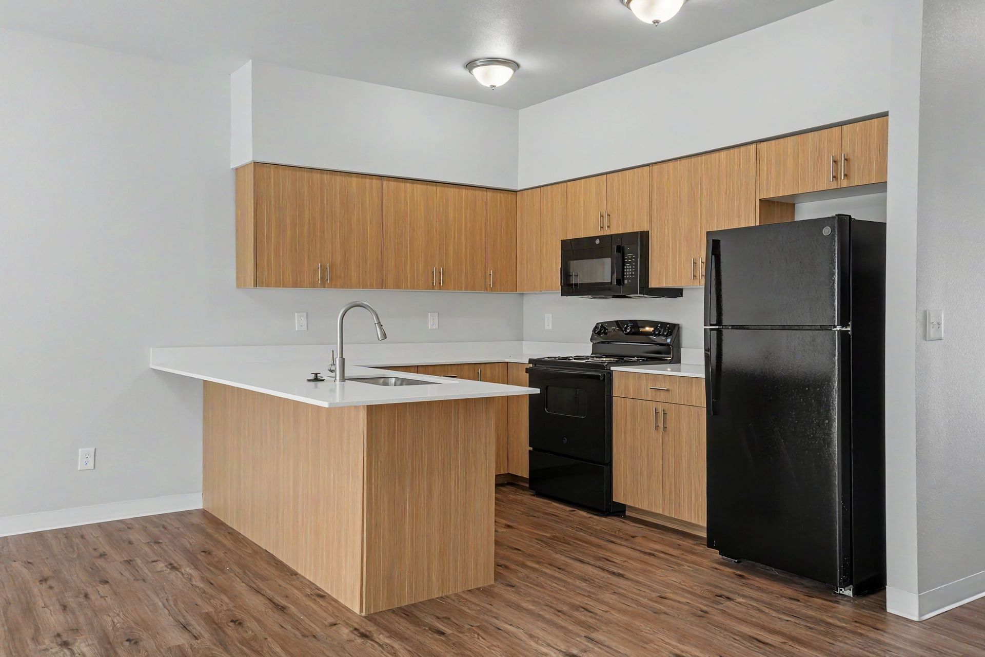 Empty modern kitchen with wood cabinets, white countertops, black appliances, and wood flooring