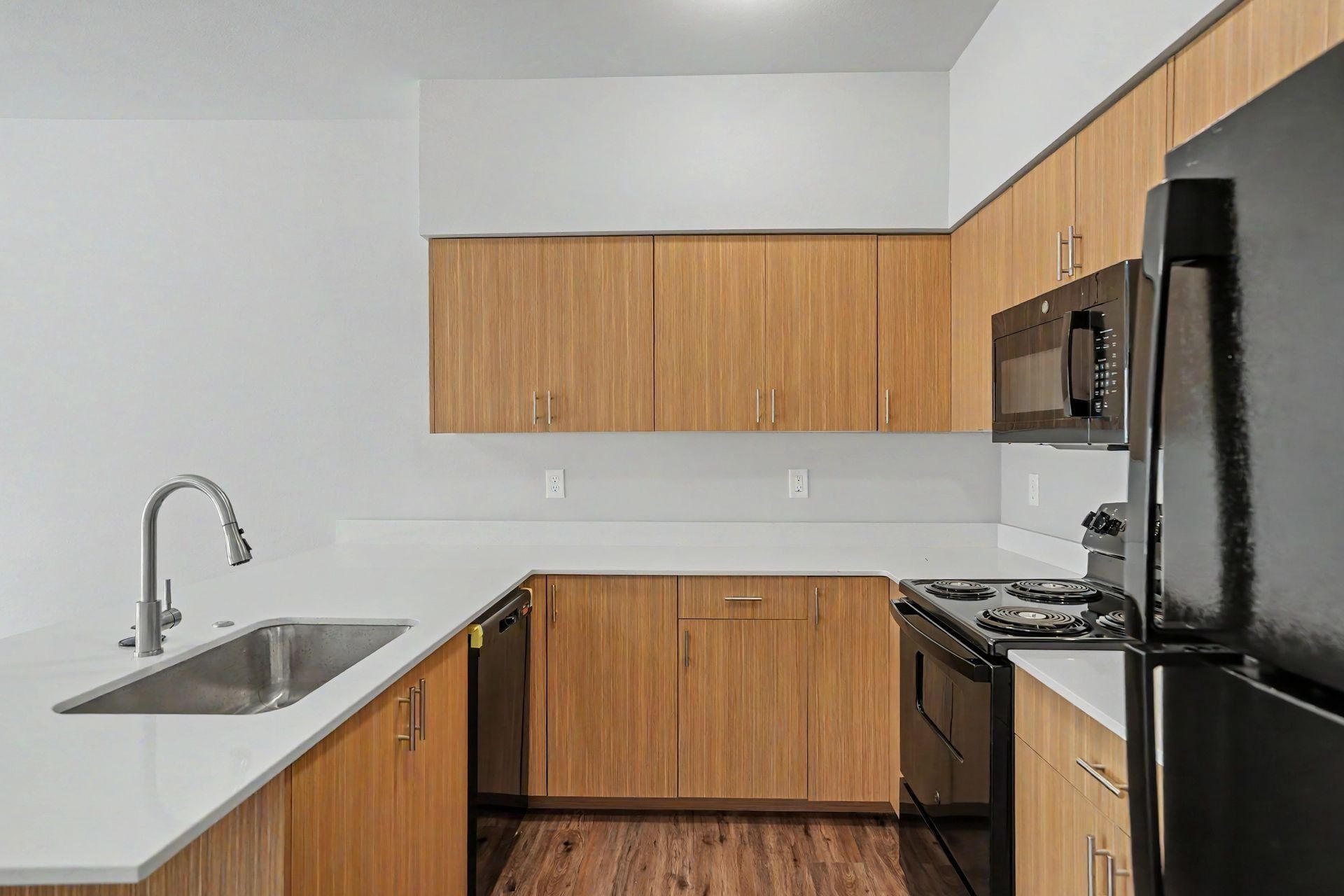 Modern kitchen with white countertops, wood cabinets, black appliances, and hardwood floor