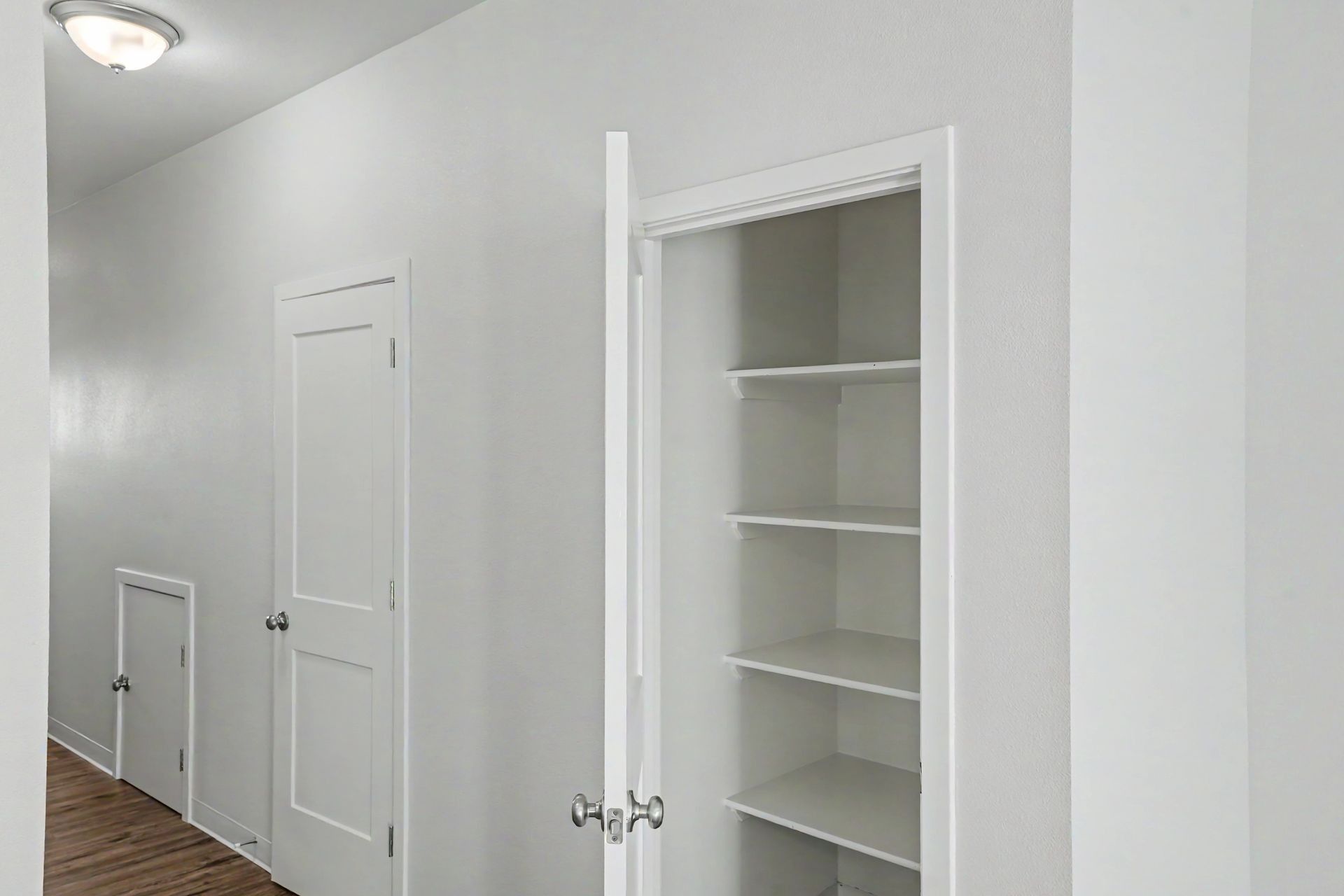 White hallway with an open closet and built-in shelves next to a closed door and small wall hatch.
