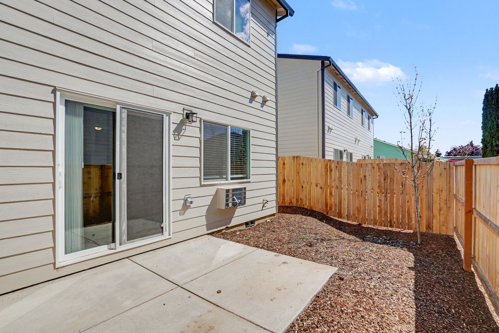 Back patio with sliding glass door, concrete slab, gravel, and wooden privacy fence beside house