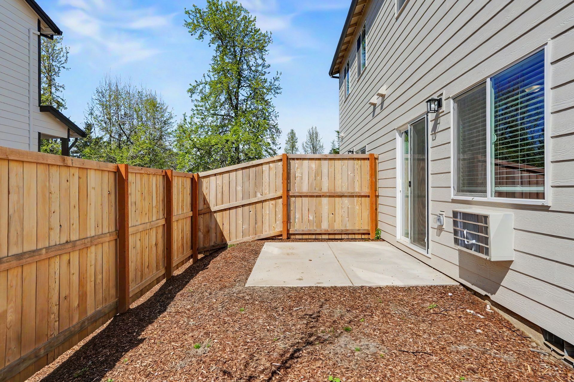 Wood-fenced side yard with gravel ground beside a gray house and windows