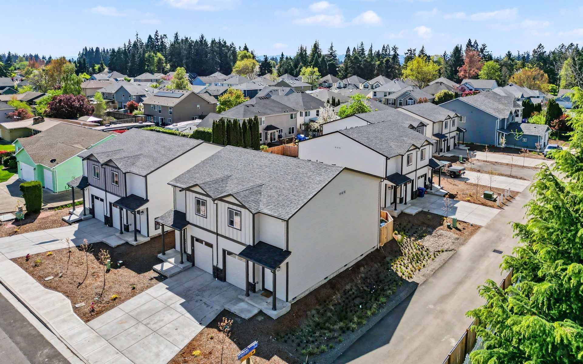 Aerial view of a suburban neighborhood with rows of newly built white houses and tree-lined streets.