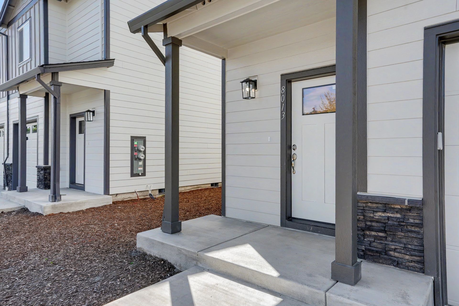 Apartment building entrance with covered porch, gray door, and stone accents along a gravel walkway