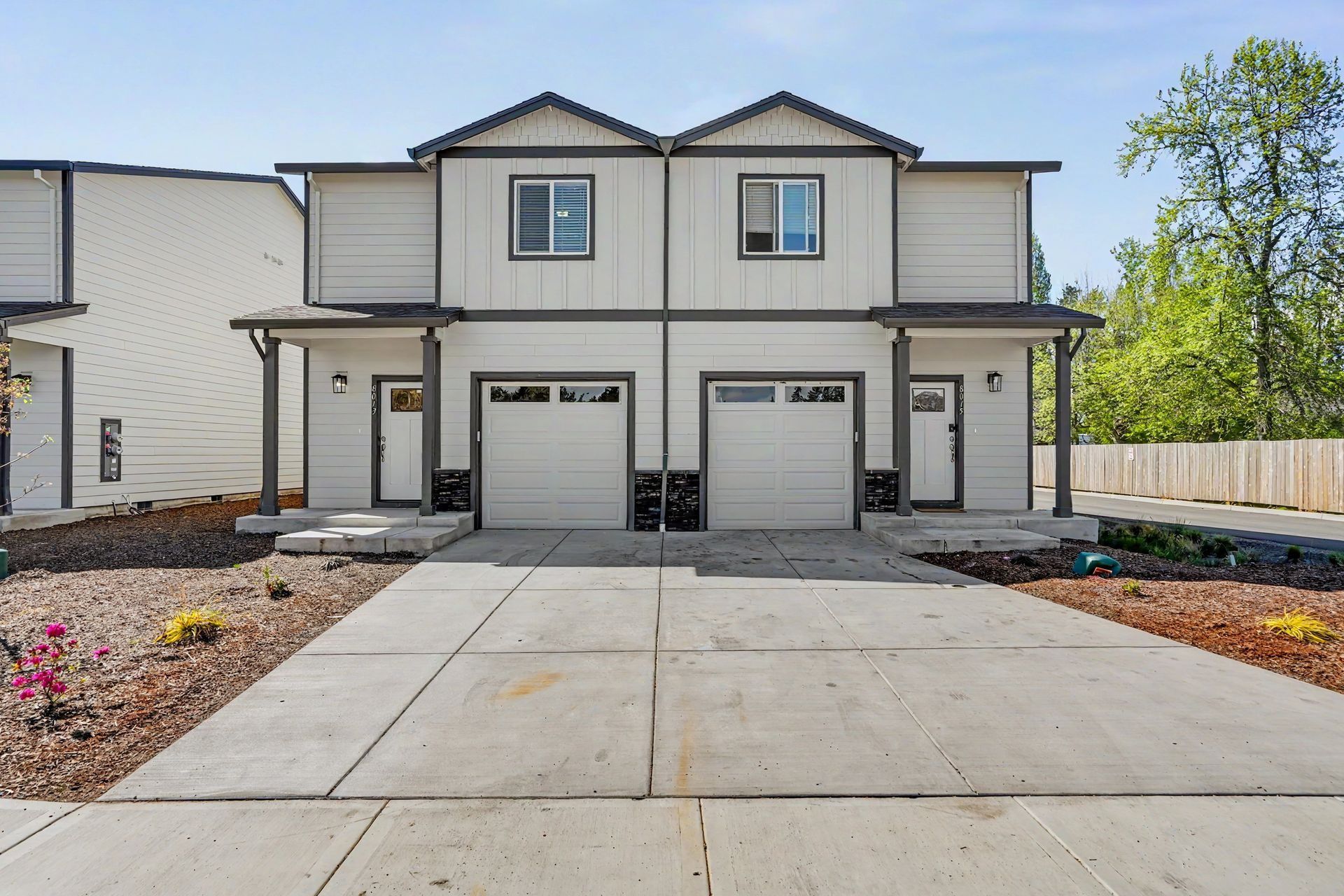 Two-story duplex with white siding, two garages, and a wide concrete driveway under a clear sky