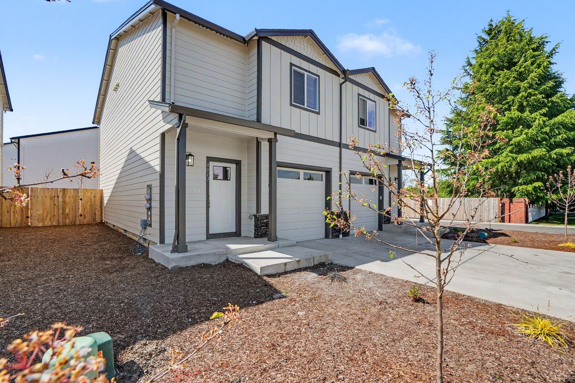 New beige two-story townhouse with a small front yard and driveway under construction
