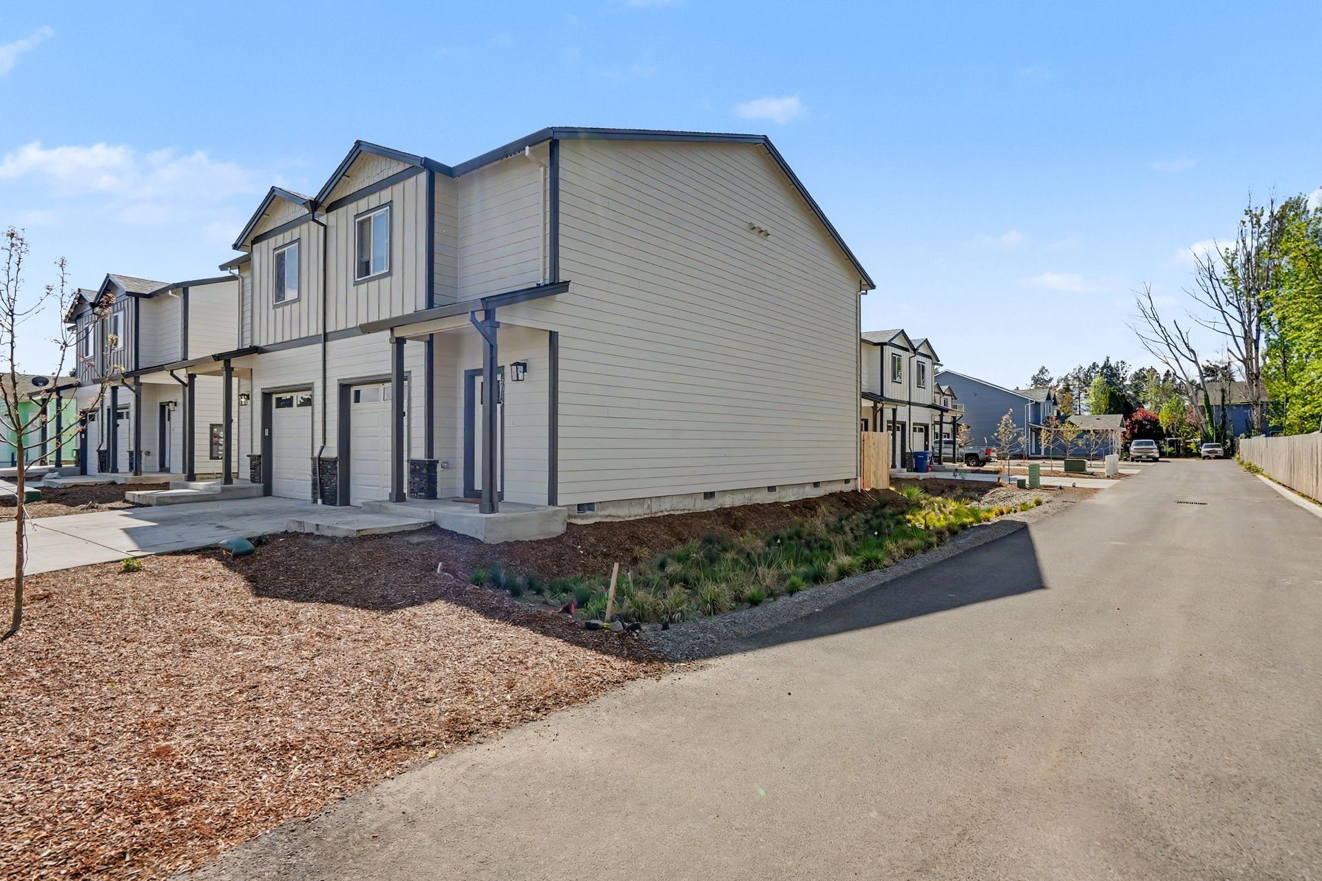 Residential street with beige townhouses, sidewalk, and landscaped gravel beds under a clear blue sky