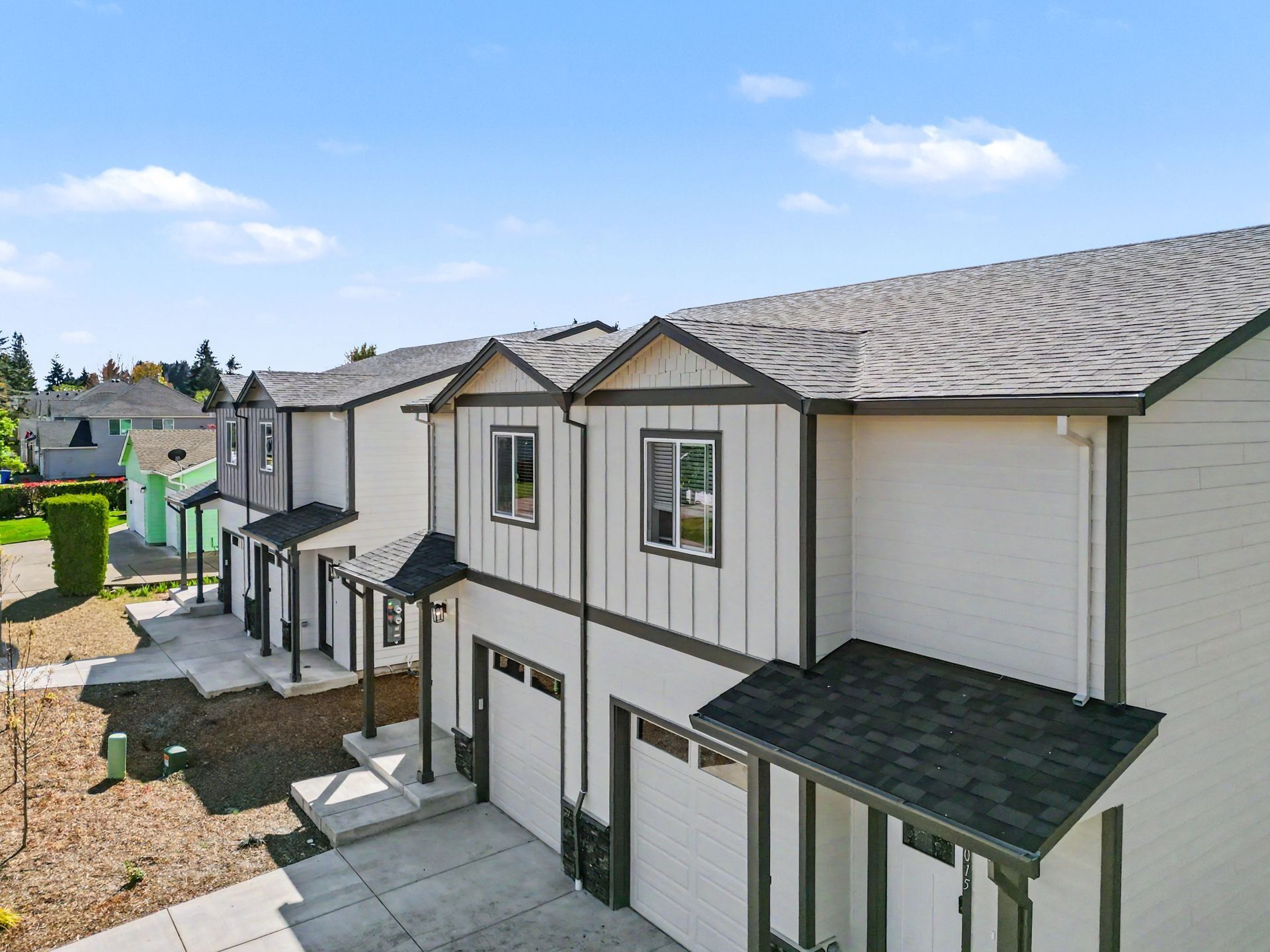 Row of beige townhouses with dark roofs, balconies, and garages on a sunny day