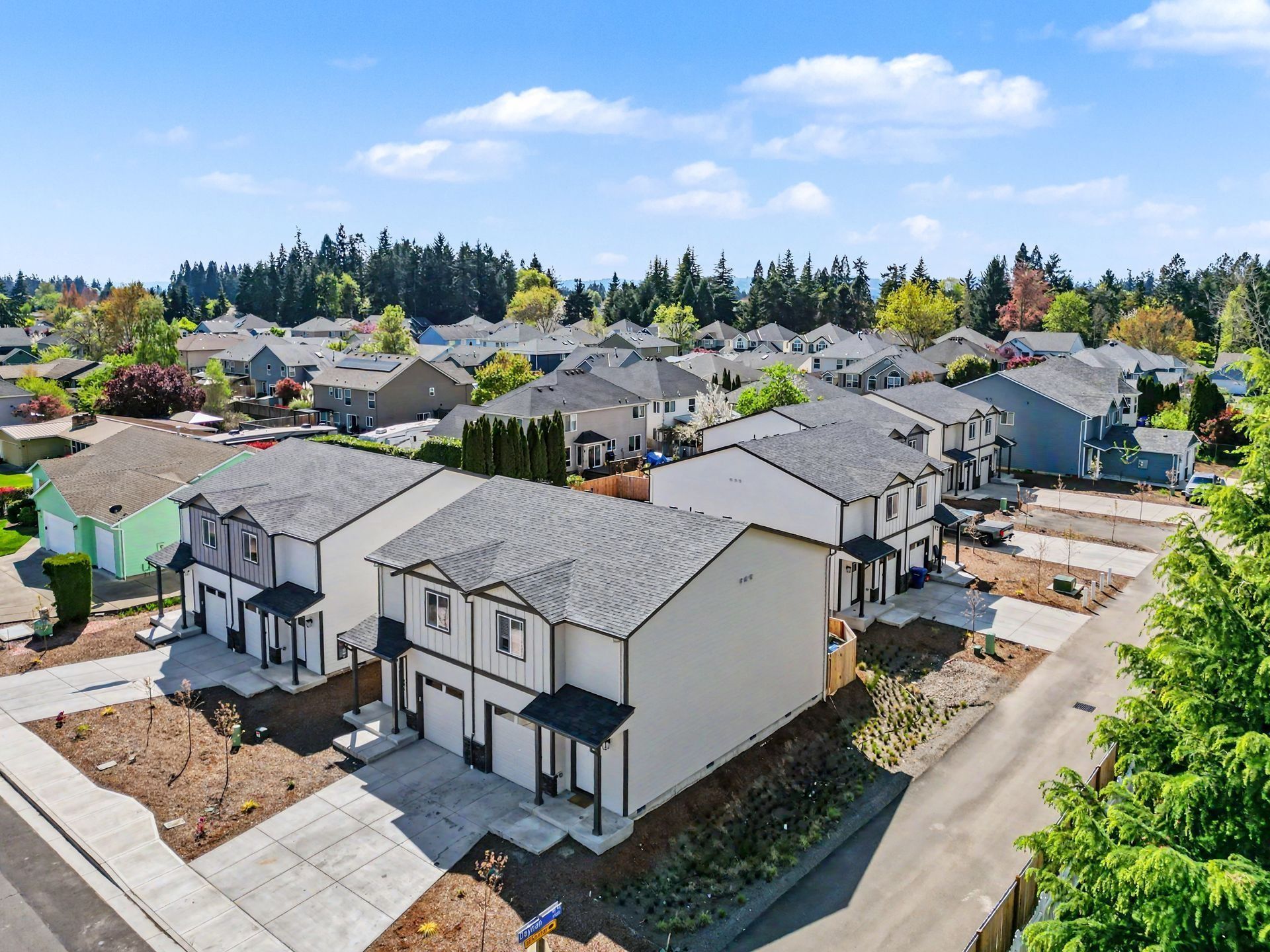 New suburban homes under construction in a sunny neighborhood, with paved roads and trees nearby
