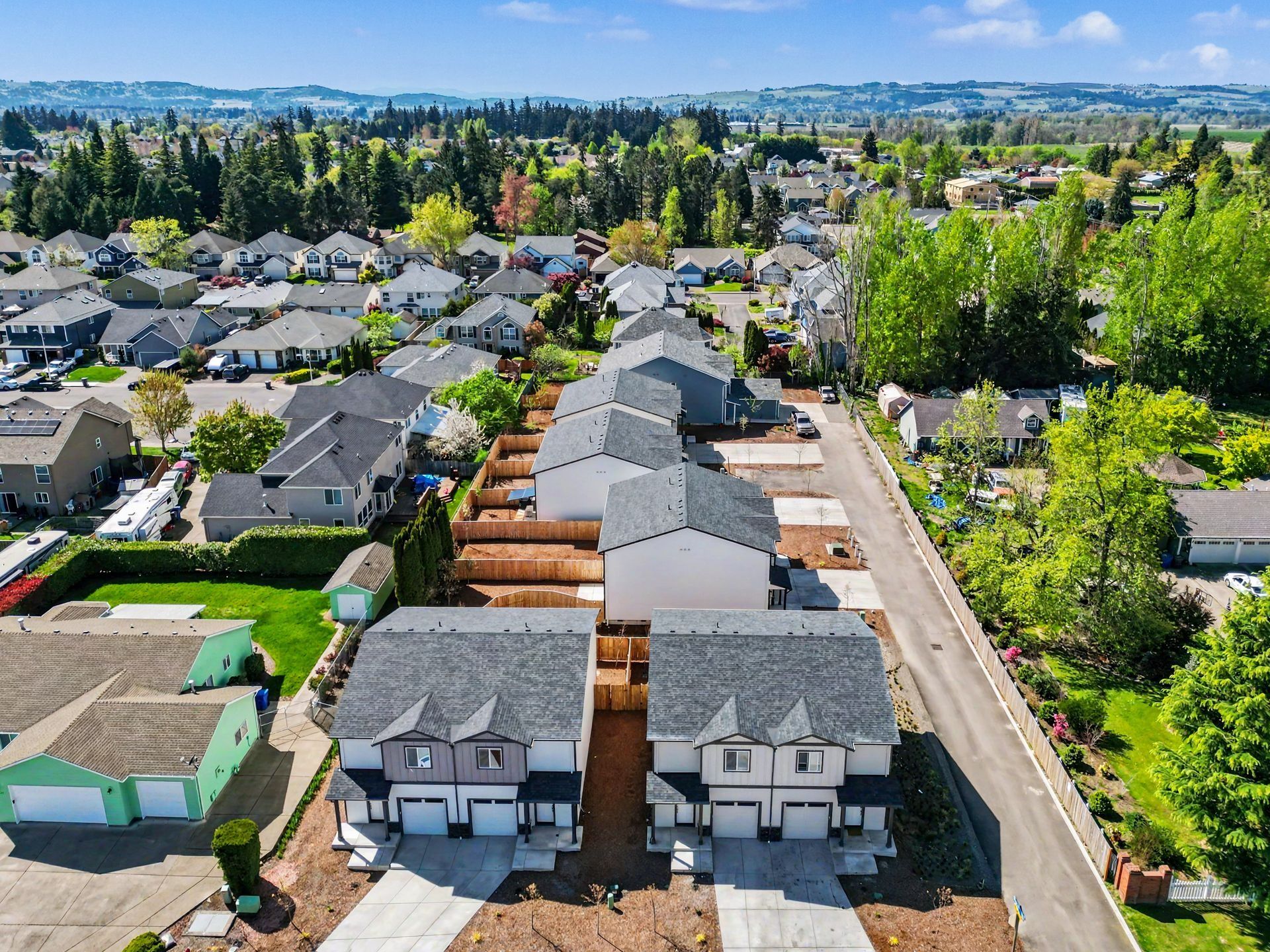 Aerial view of a suburban neighborhood with rows of townhouses, trees, and distant city skyline.