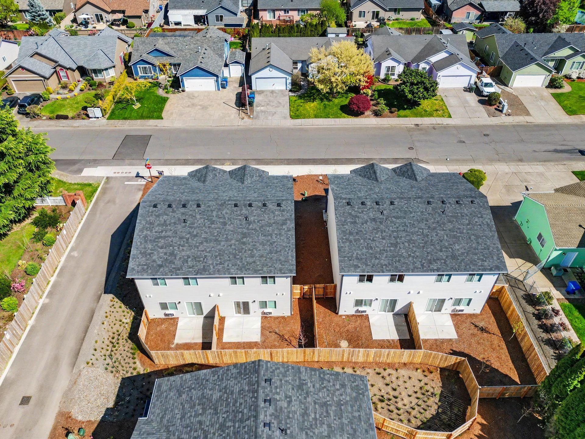 Aerial view of two newly built white houses with dark roofs and a paved courtyard.