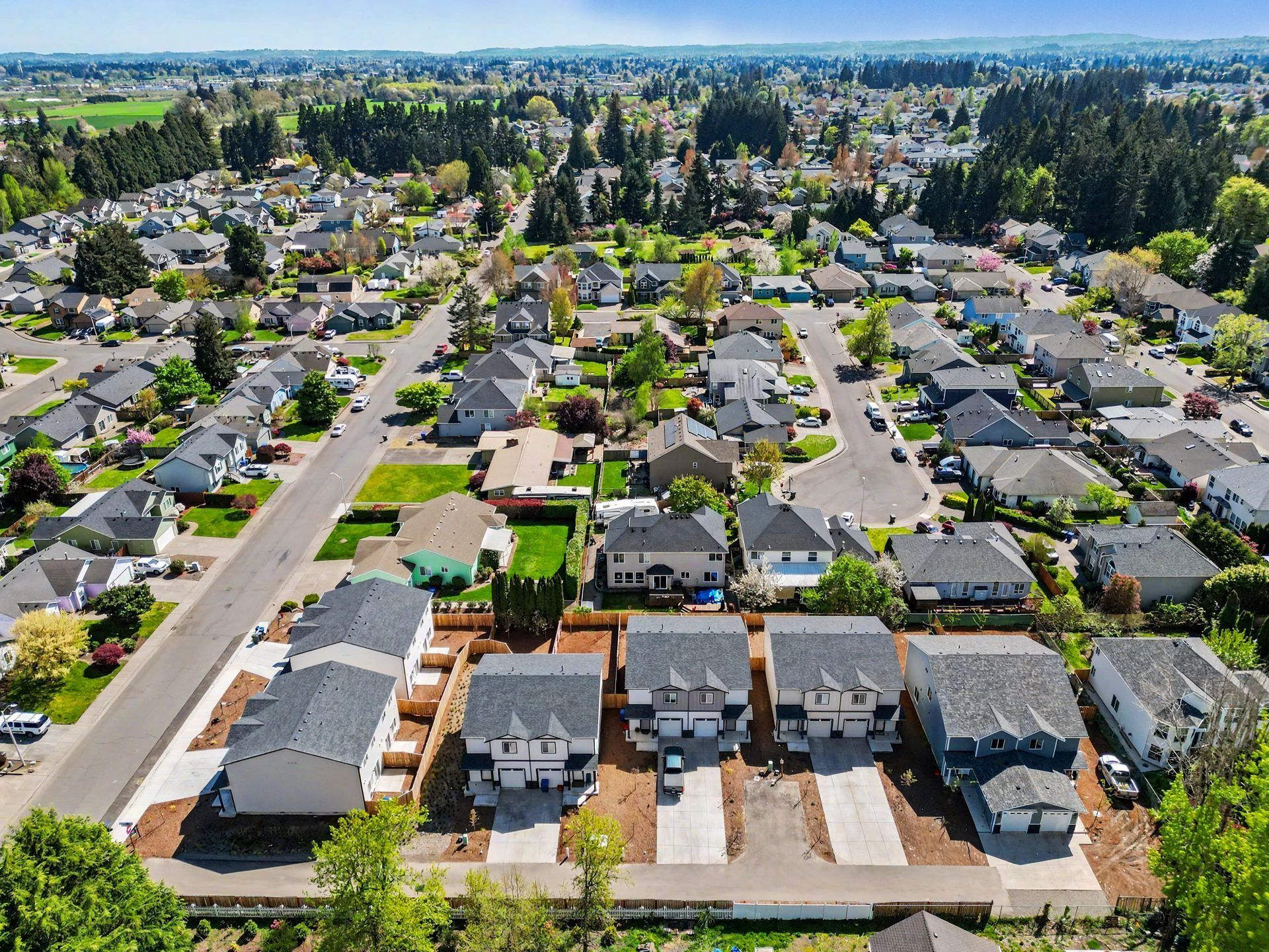 Aerial view of a suburban neighborhood with rows of houses, streets, and trees under a clear sky