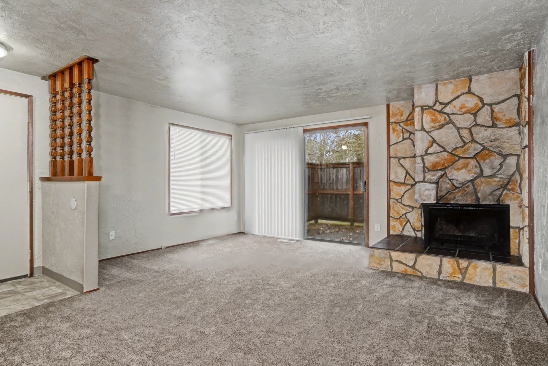 Empty living room with carpet, stone fireplace, sliding glass door, and white walls