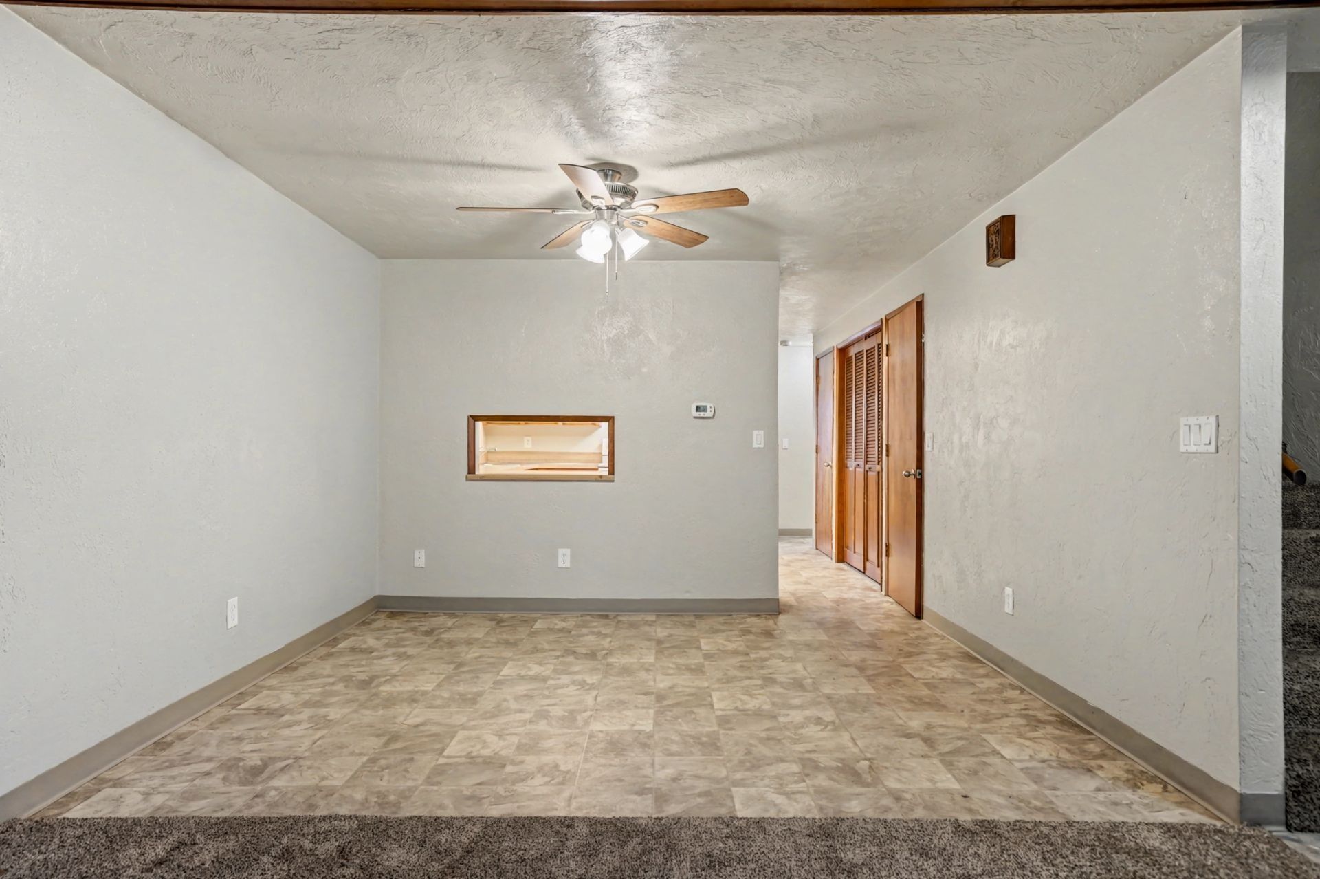 Empty living room with gray walls, carpeted floor, ceiling fan, and wood closet doors.