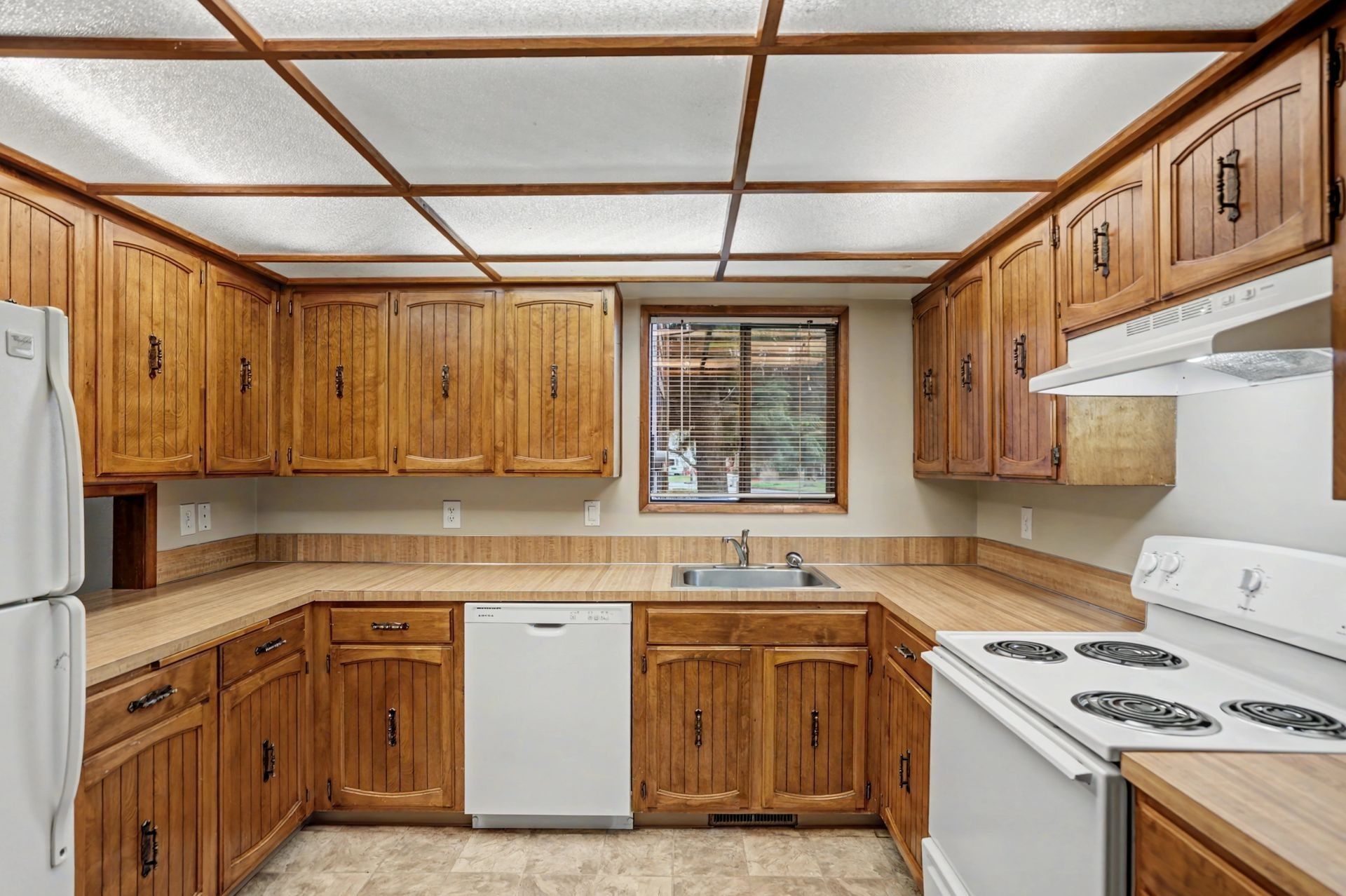 Wood-paneled kitchen with white appliances, beige countertops, and tiled floor