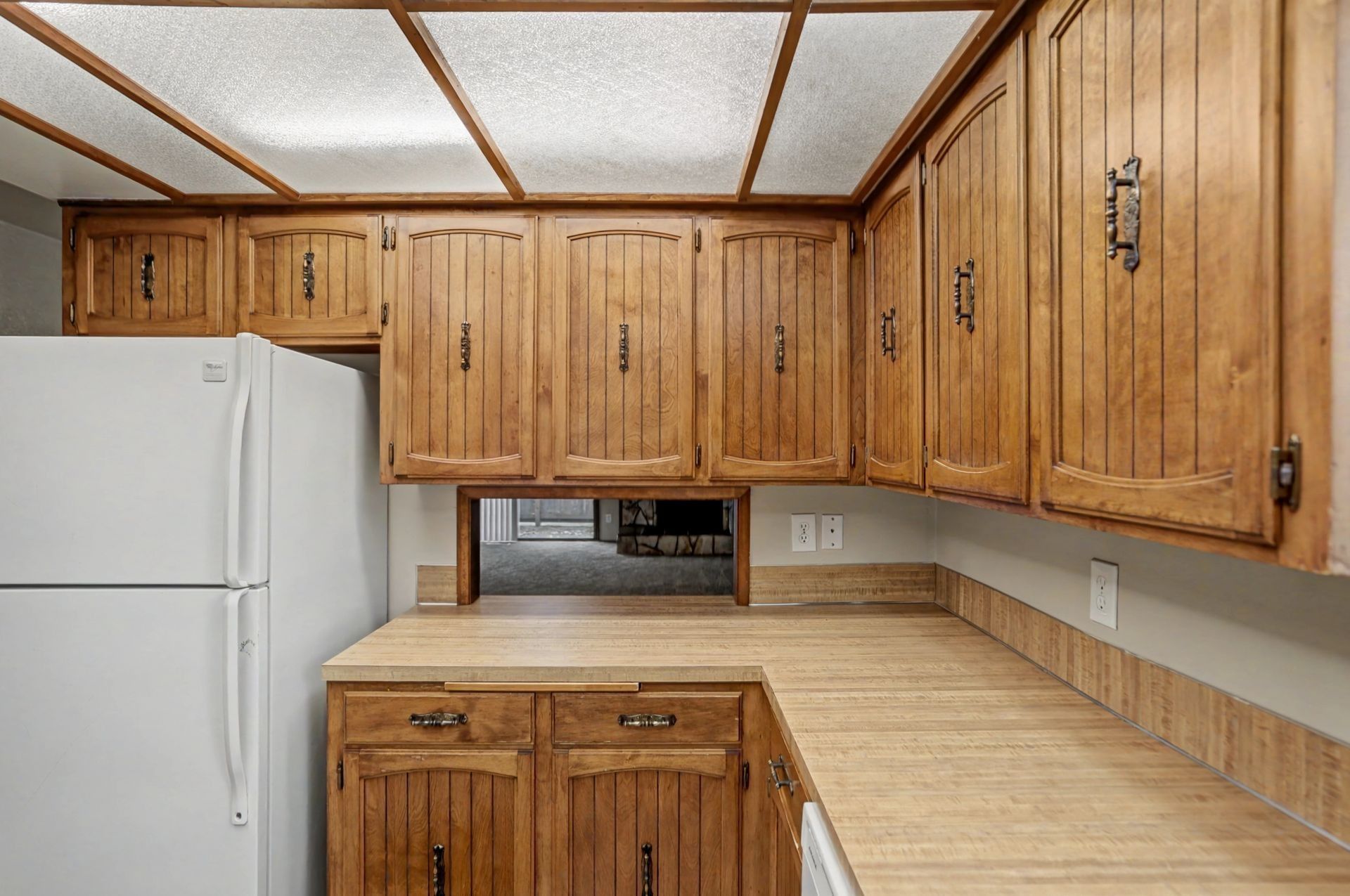 Small kitchen with wood cabinets, beige counters, white appliances, and fluorescent ceiling panels