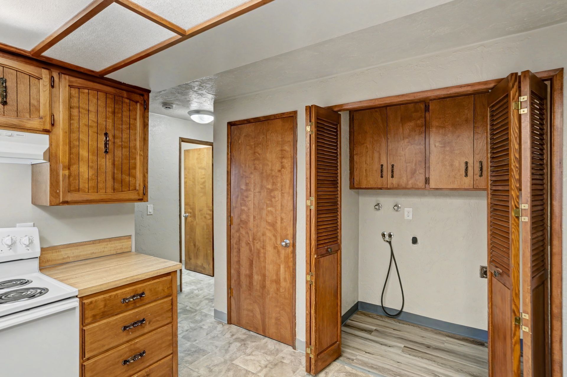 Small kitchen with wood cabinets, white stove, tiled floor, and an empty laundry nook.