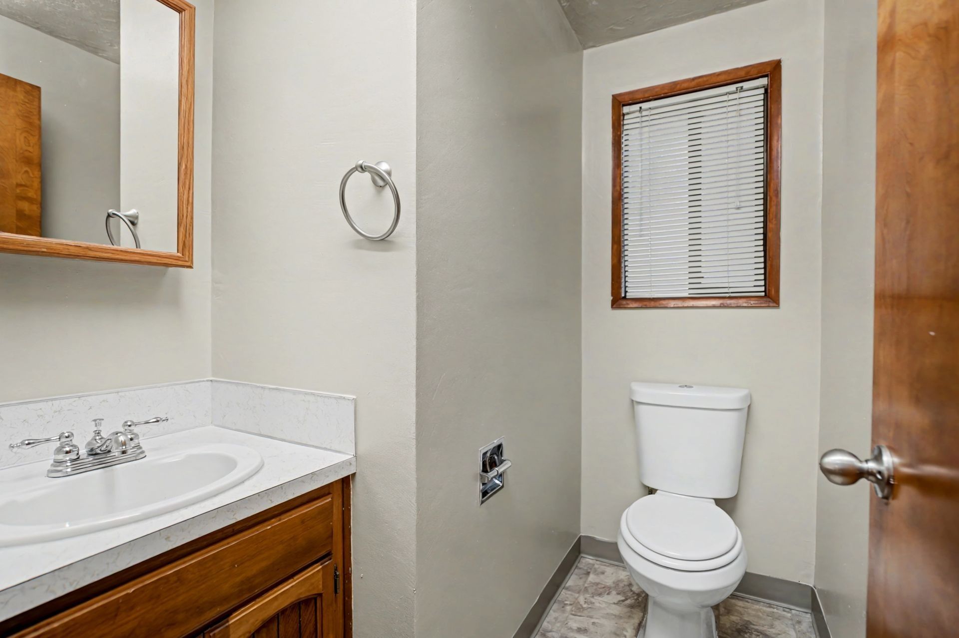 Small bathroom with vanity, mirror, toilet, and window blinds.