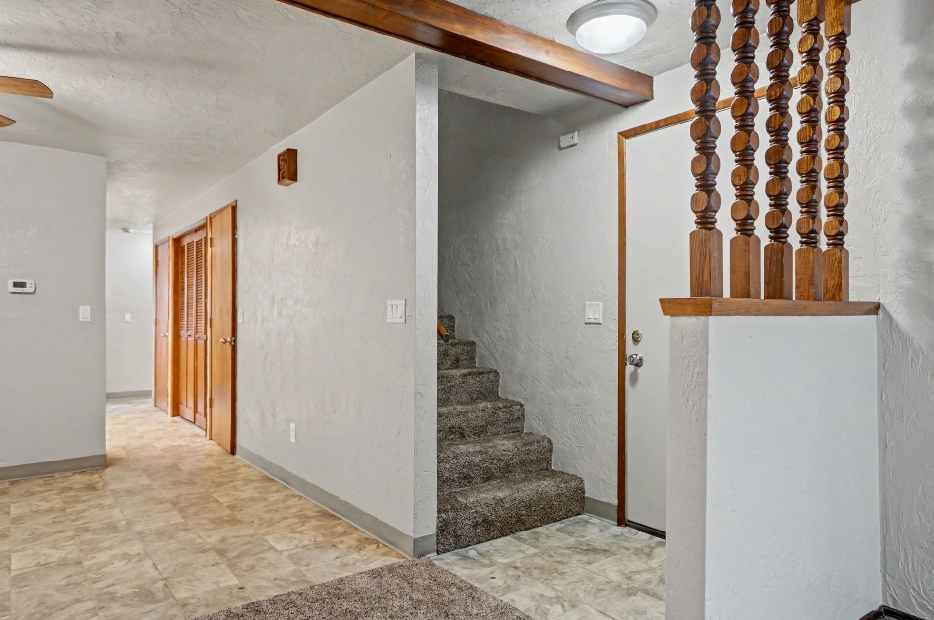 Interior hallway with carpeted stairs, wooden railing, and tiled floor in a home