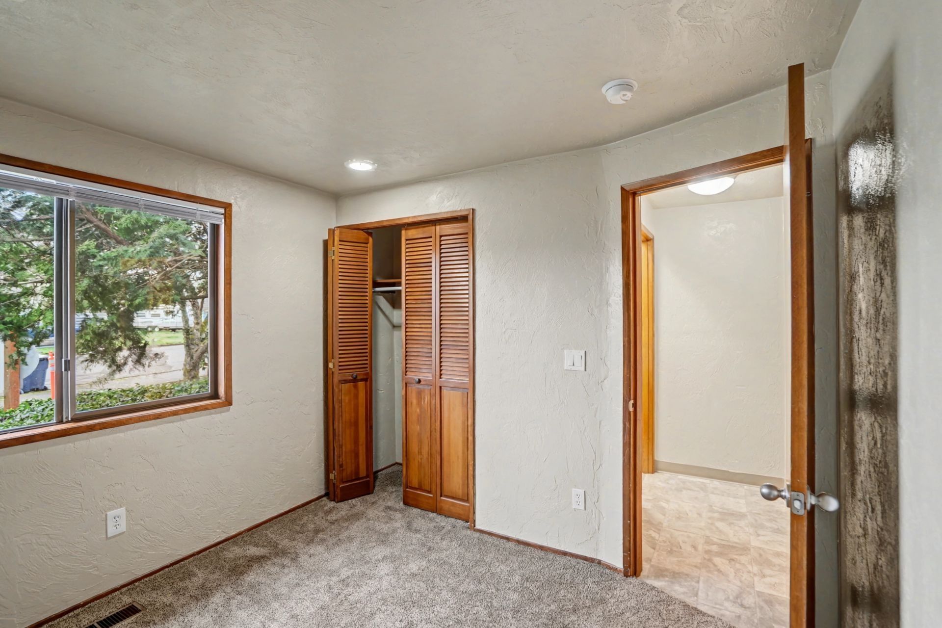 Empty carpeted bedroom with a closet, window, and open doorway into a hallway