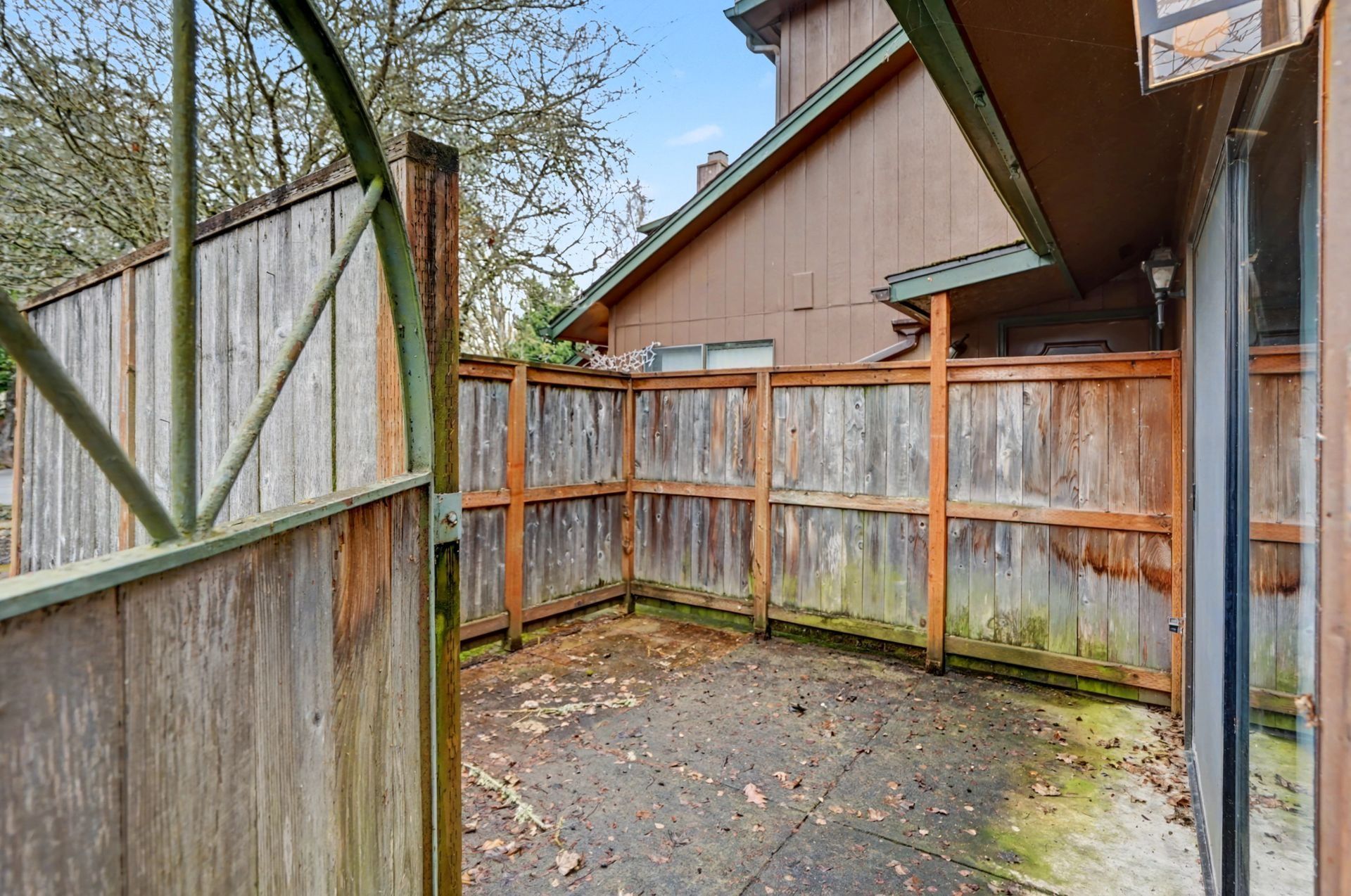 Small fenced backyard patio with weathered wooden privacy fence and concrete ground.