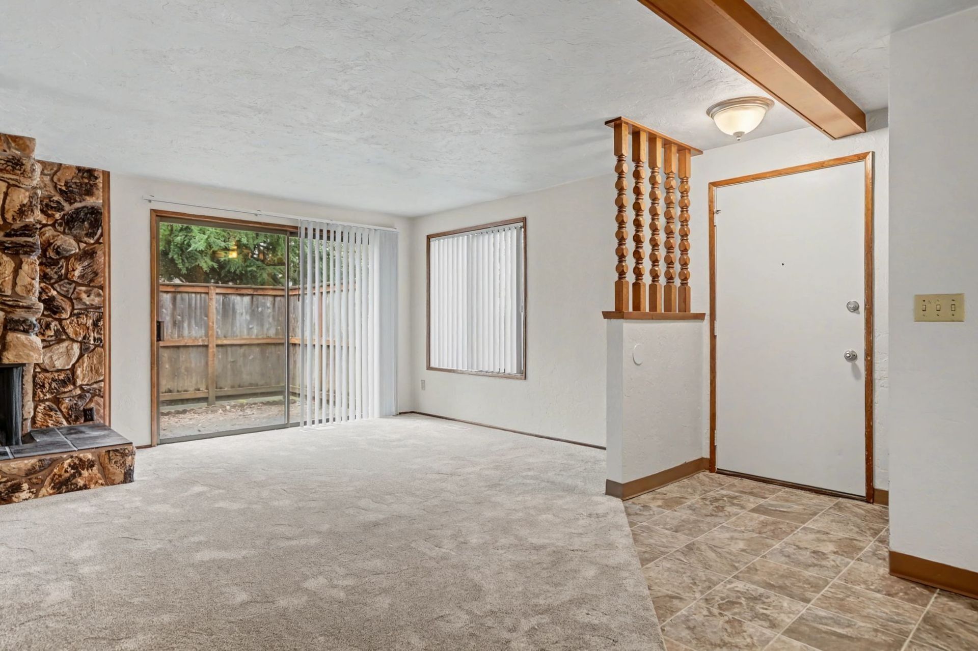 Empty living room with beige carpet, fireplace, sliding glass door, and white front door.