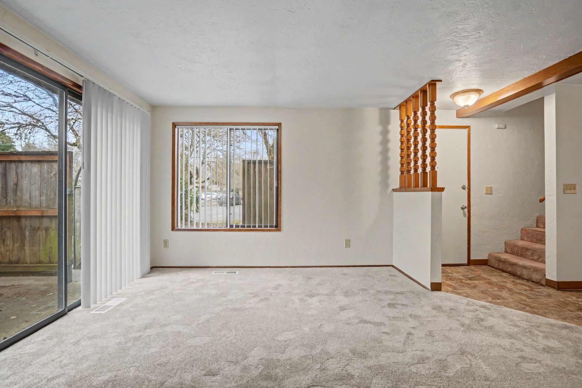 Empty living room with carpet, large sliding glass door, window, and staircase to the right