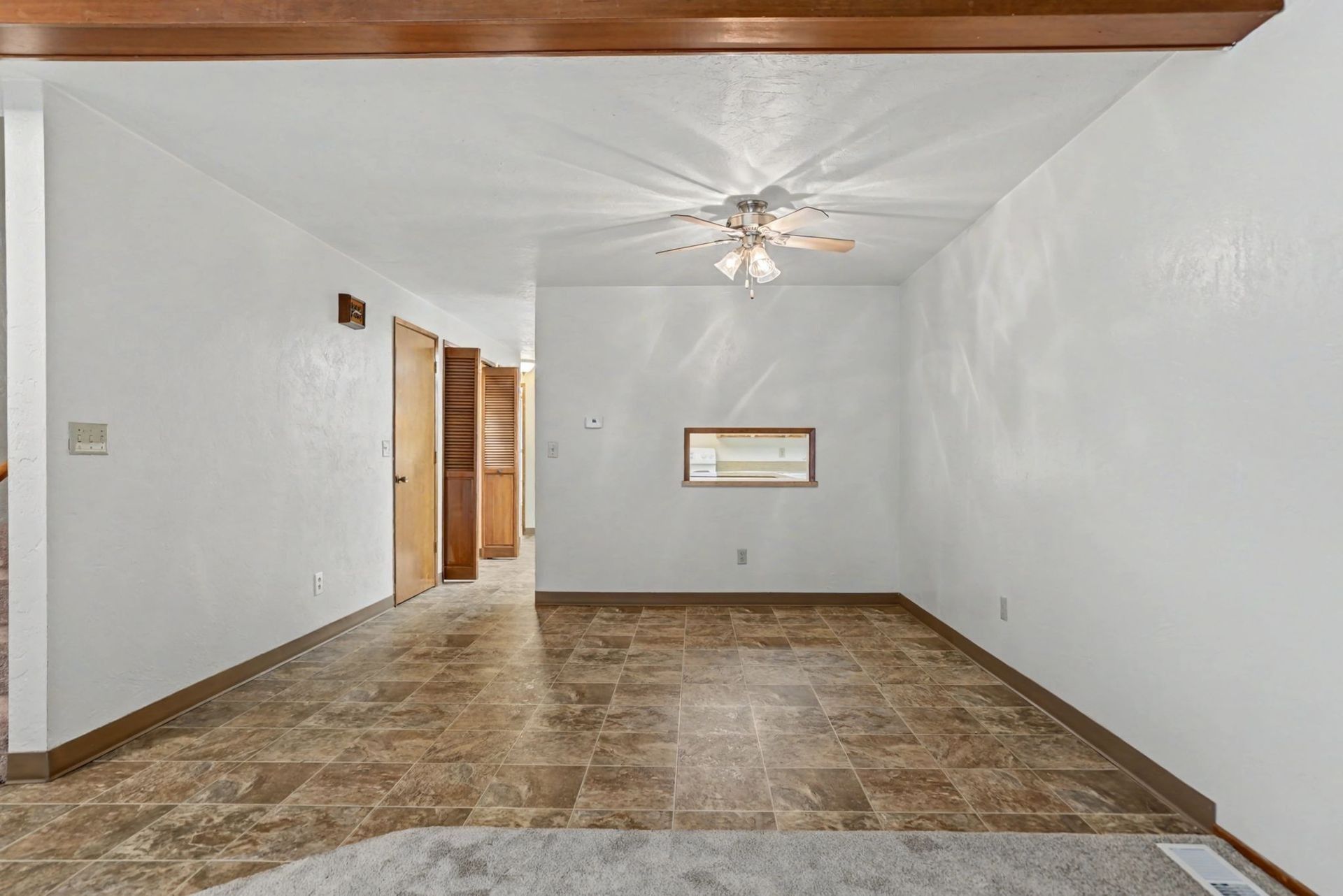 Empty living room with white walls, tiled floor, ceiling fan, and a doorway to the left.