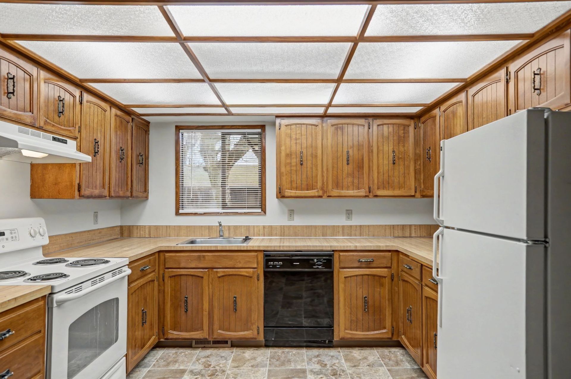 Kitchen with wooden cabinets, white appliances, tiled backsplash, and a window above the sink.