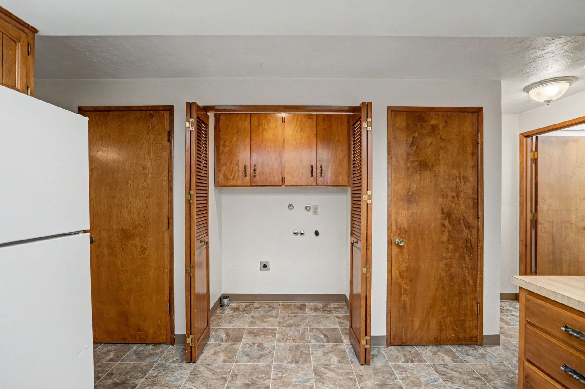 Empty kitchen nook with wood cabinets, white fridge, tiled floor, and closed wood doors on both sides