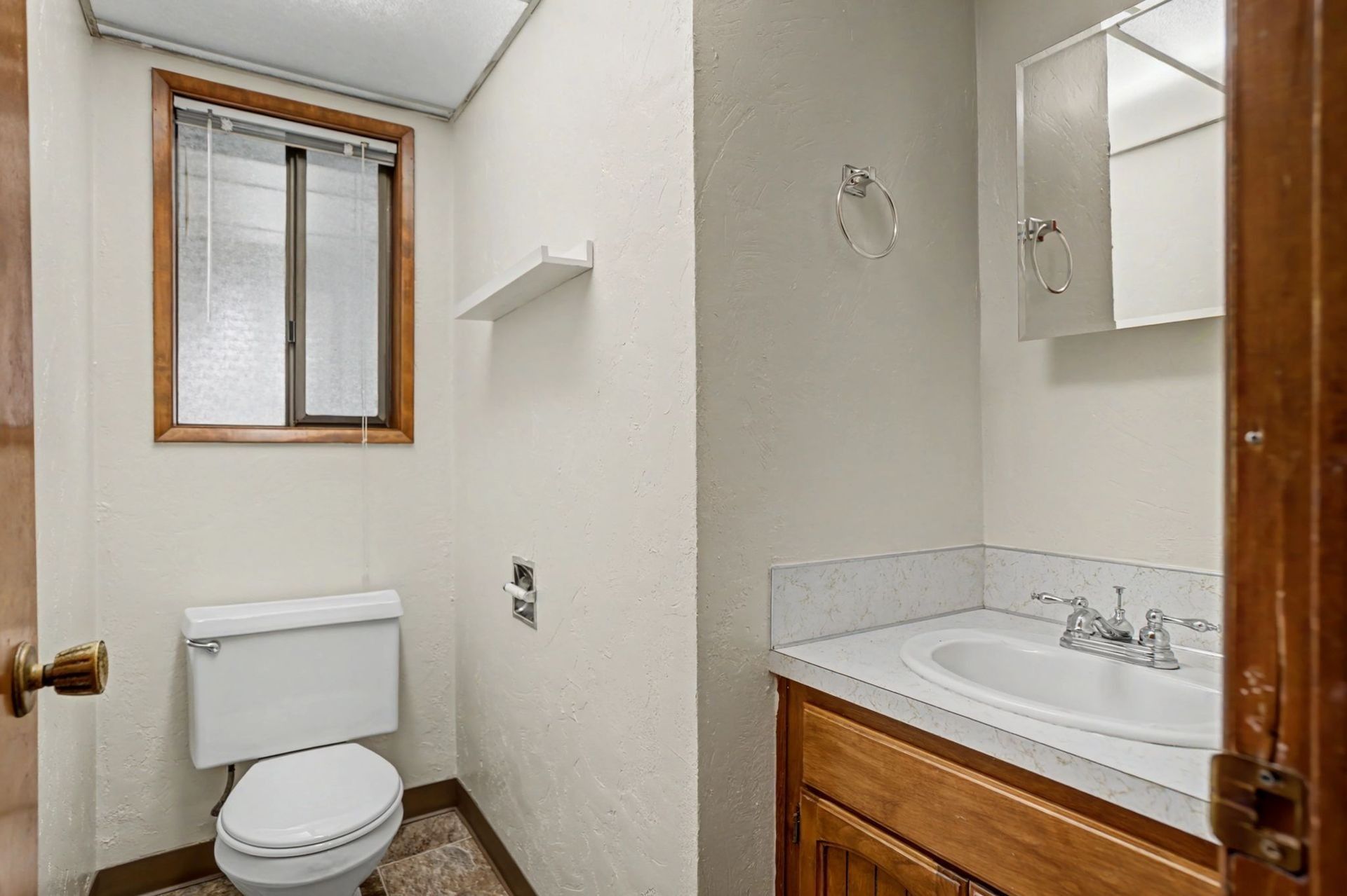 Small bathroom with toilet, window, and wood vanity with sink and mirror.