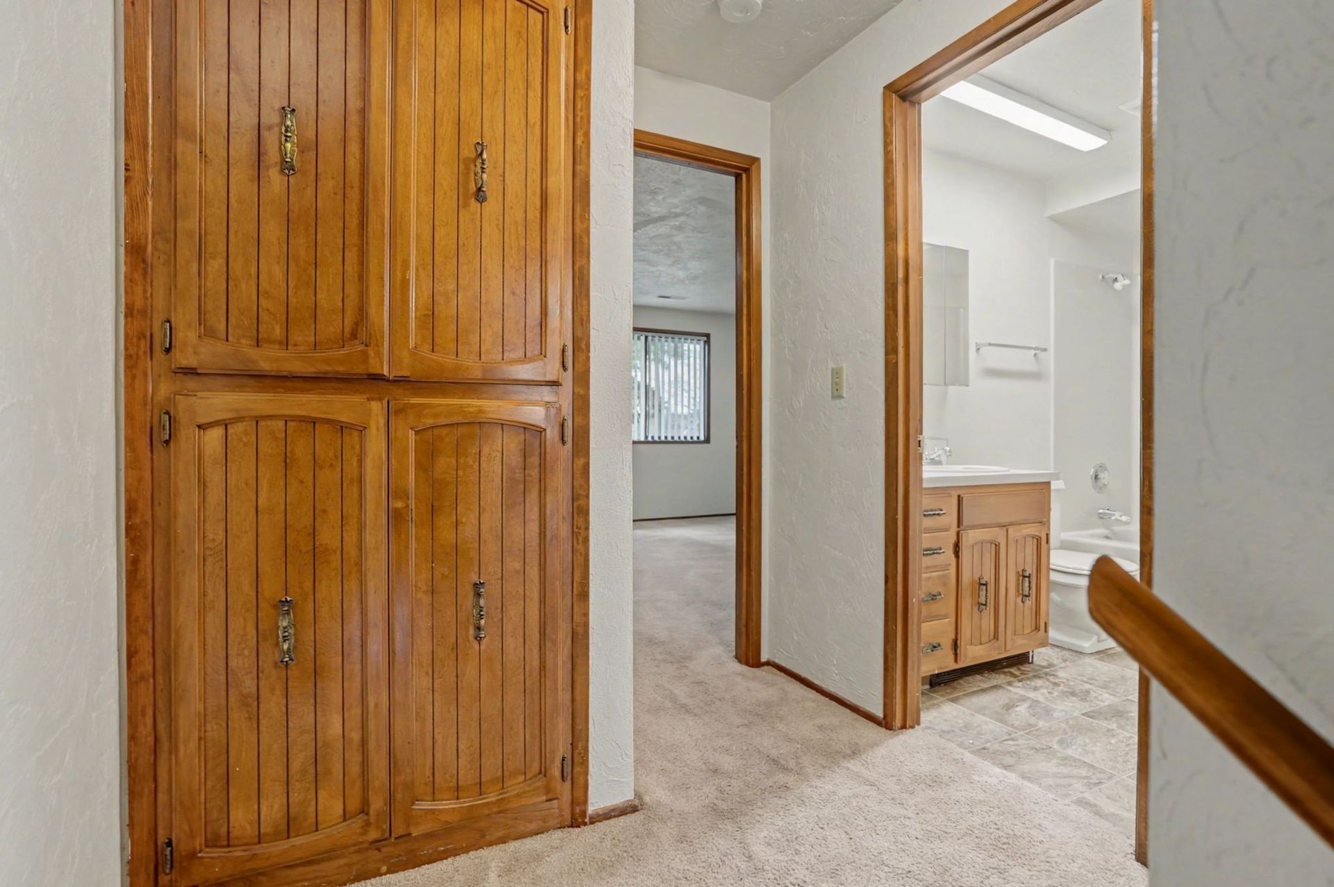 Hallway with wooden built-in cabinets, a doorway to a bathroom, and carpeted floors