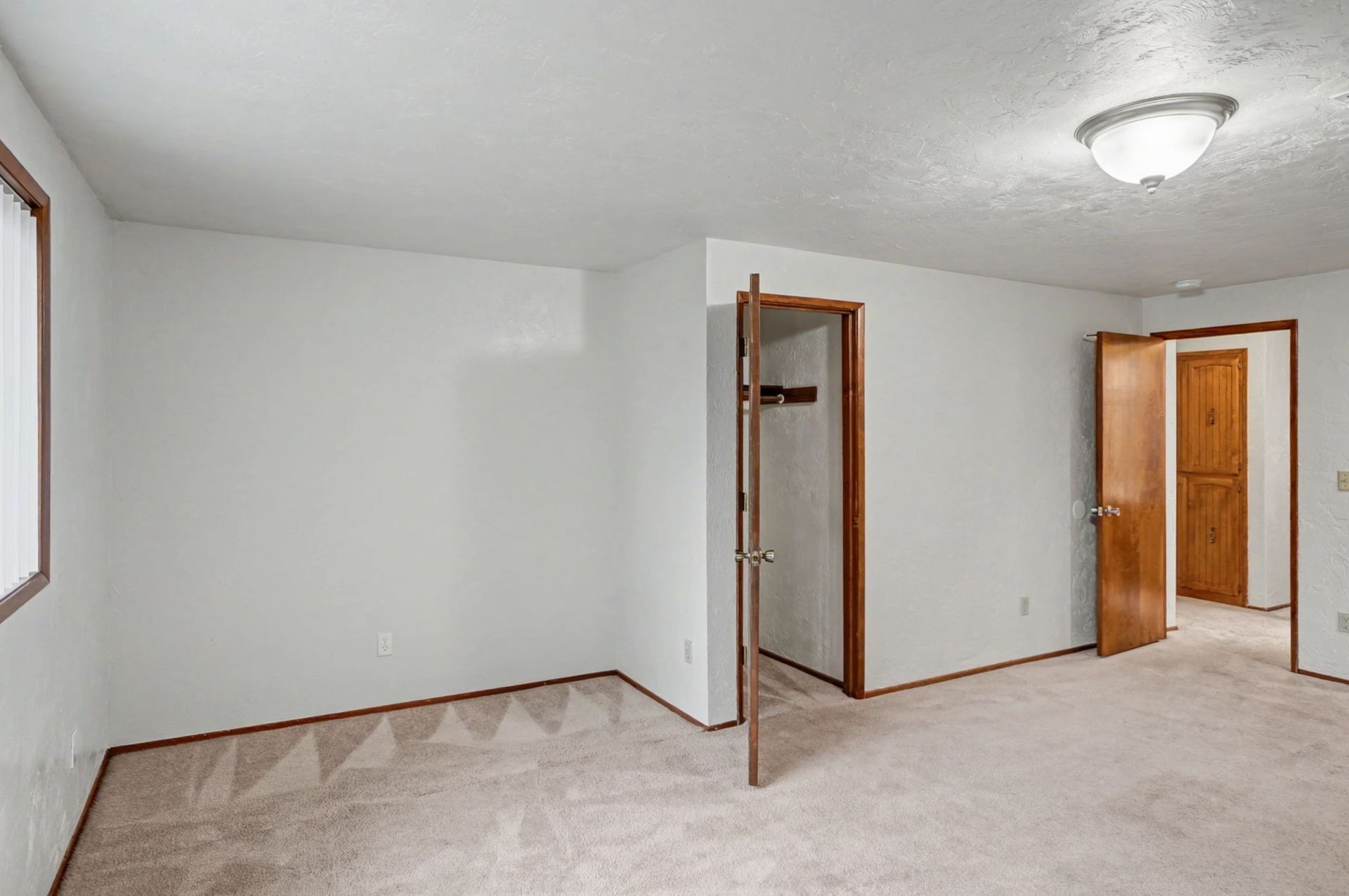 Empty beige carpeted room with white walls, open closet, and wooden doors