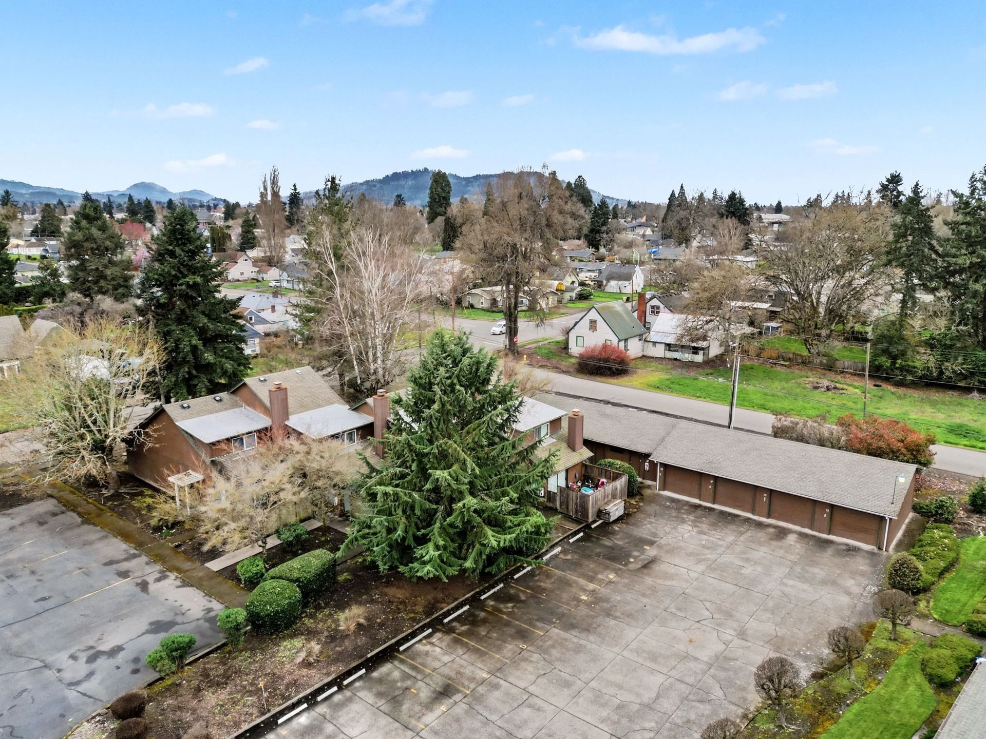 Suburban neighborhood with houses, trees, and a paved parking lot under a clear blue sky